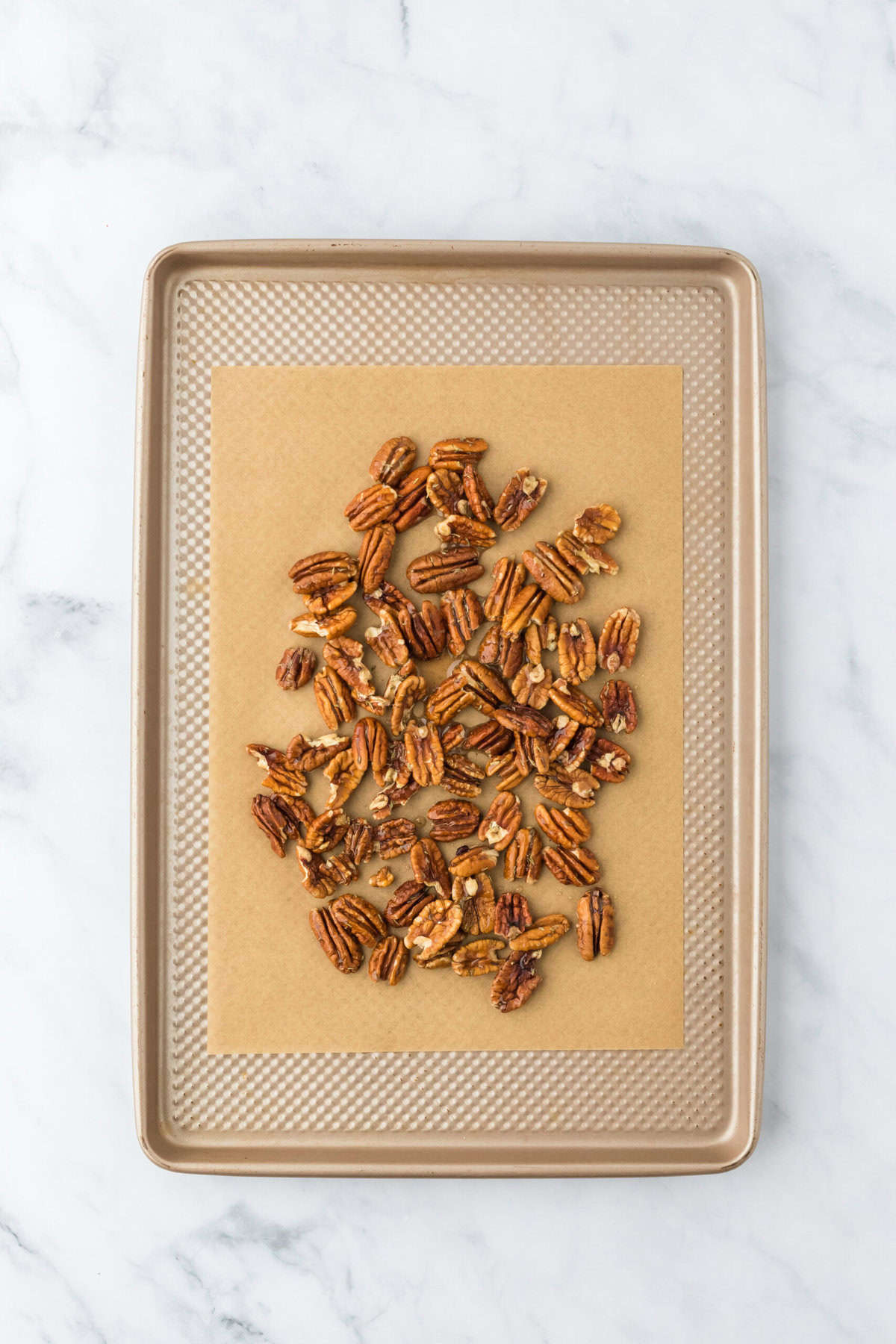 Pecans with candied wet mix poured over them on a parchment lined baking sheet