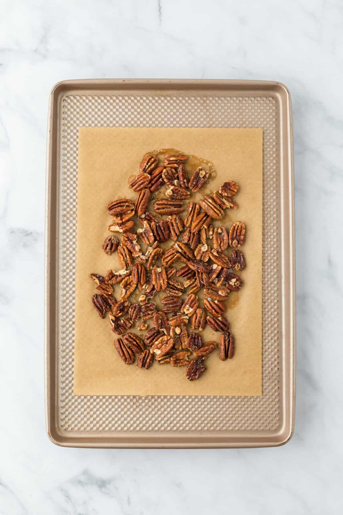 Baked candied pecans on a parchment lined baking sheet after baking