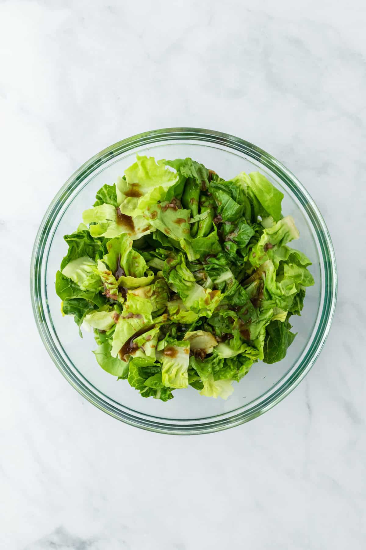 Honey balsamic vinaigrette drizzled on lettuce in a clear bowl on a white background