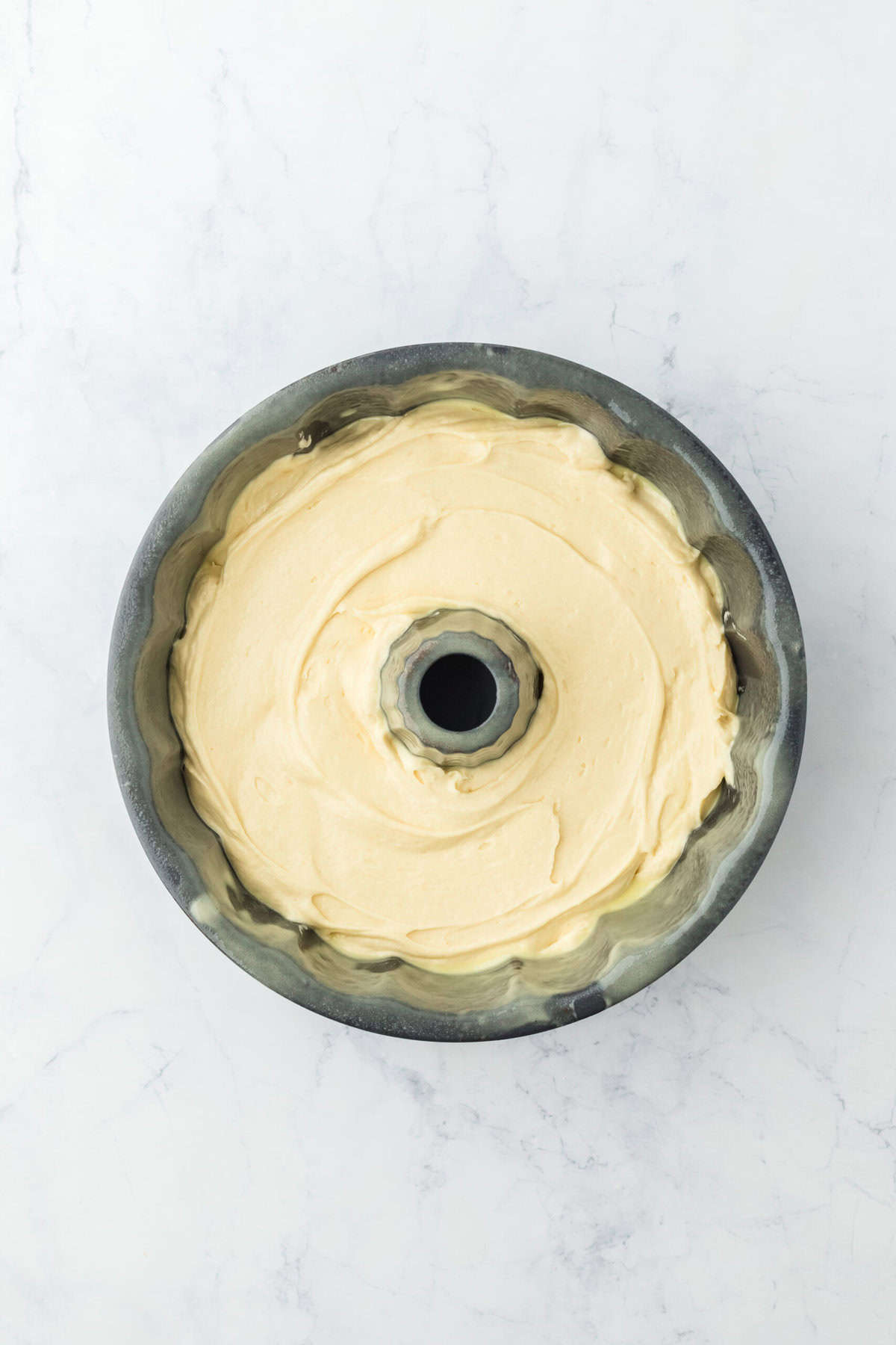 Cake batter added to bundt pan on white background