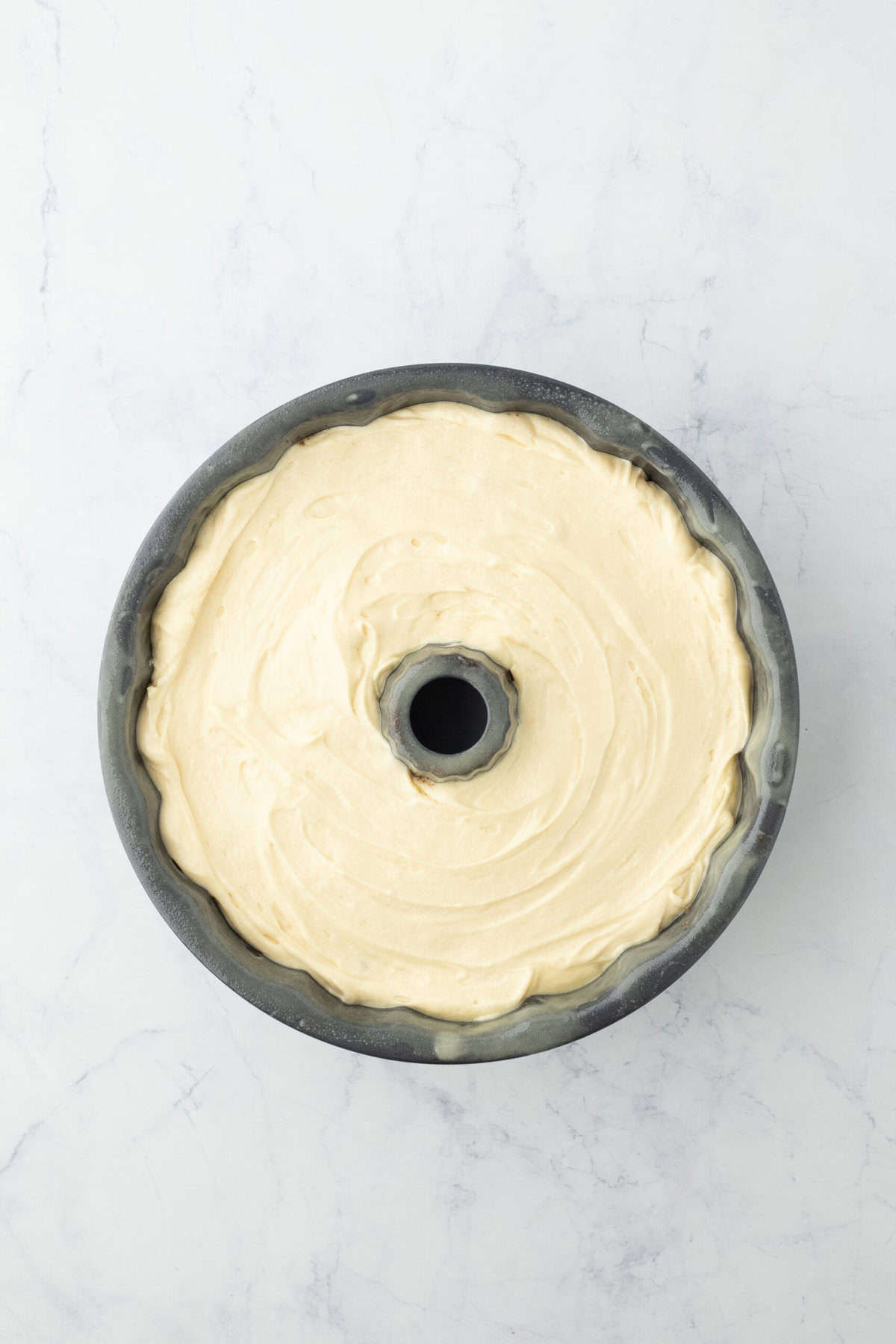 Remaining batter added to bundt pan on white background