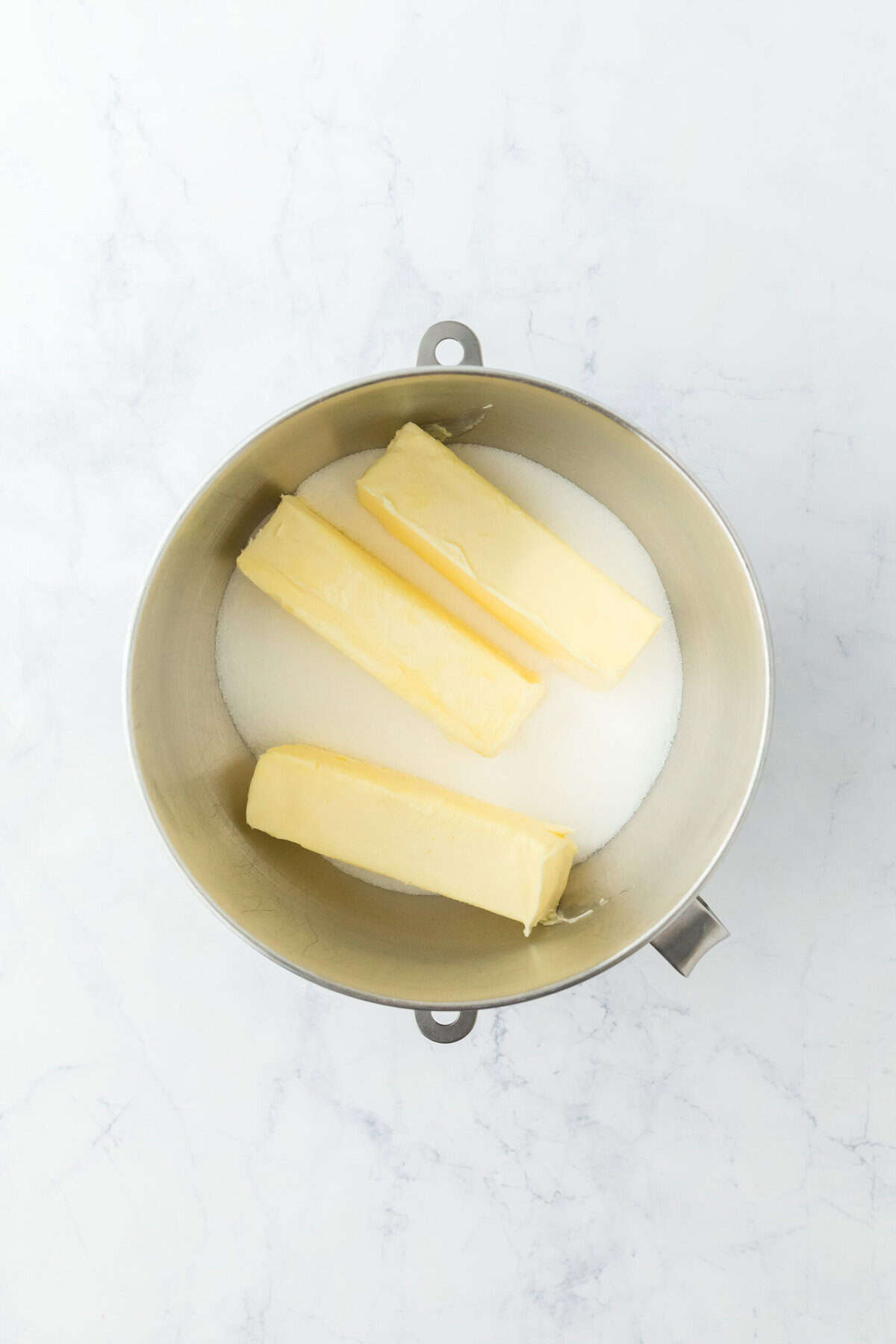 Butter and sugar in a stand mixer bowl on a white background