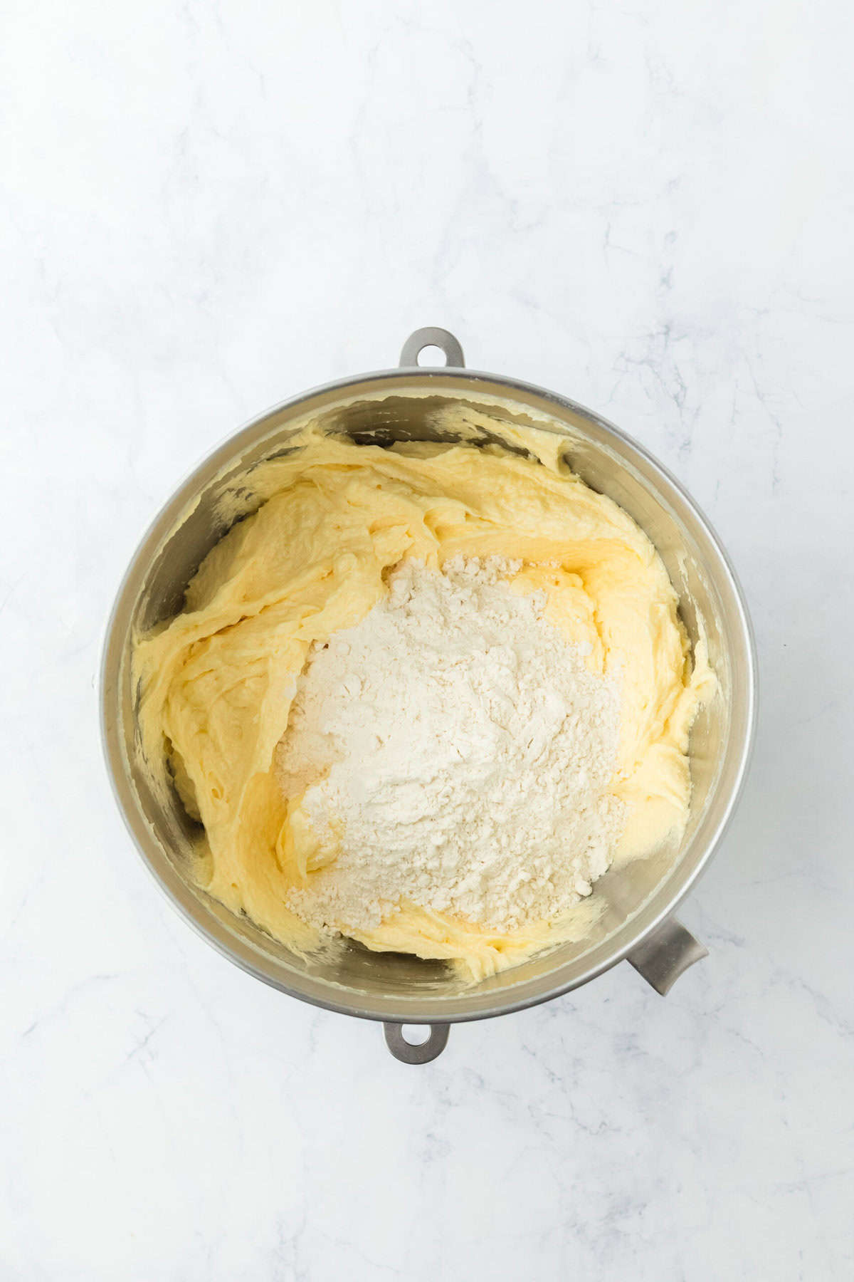 Flour added to creamed cake mixture in stand mixer bowl on white background