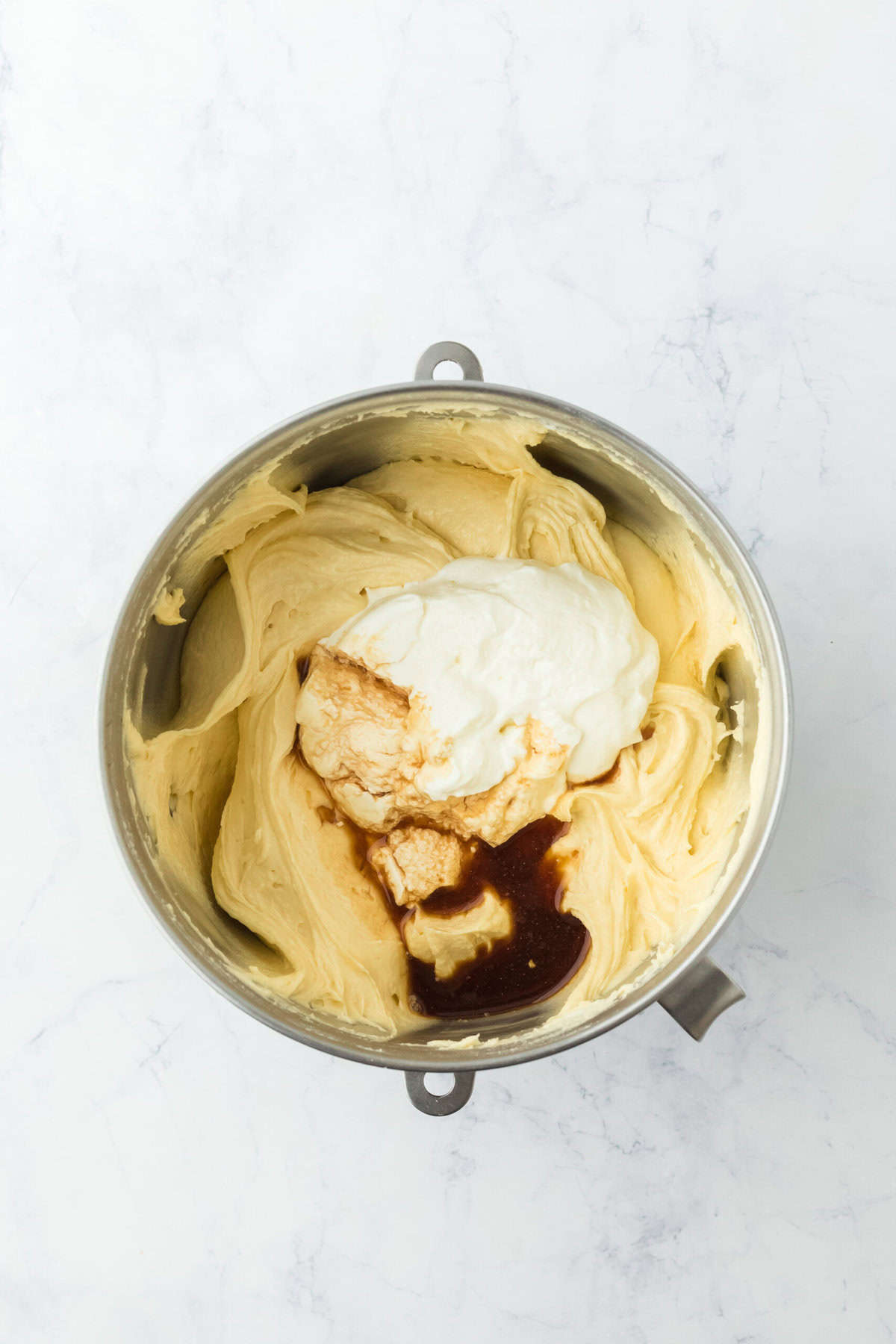 Sour cream and vanilla added to cake batter in stand mixer bowl on white background