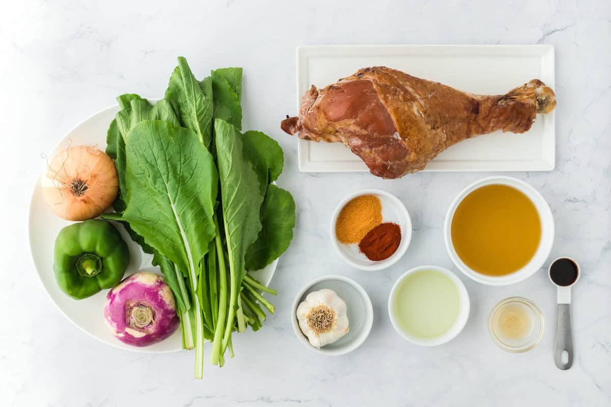 Turnip greens, a turnip, onion, green pepper, a turkey leg, spices and chicken stock on a white background to cook turnip greens