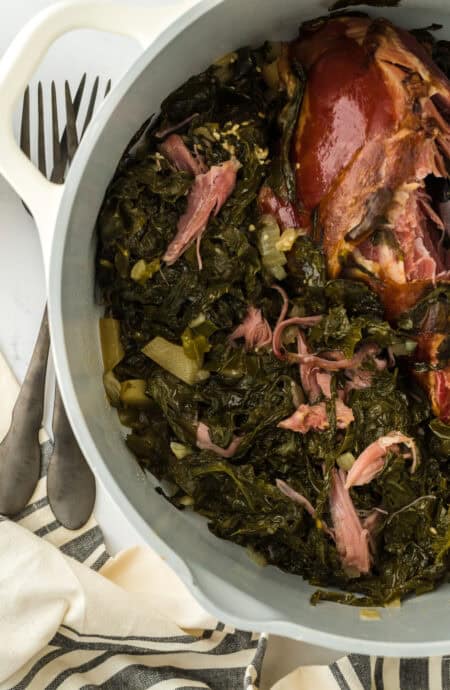 A large white pot of turnip greens with smoked turkey after cooking on a white background