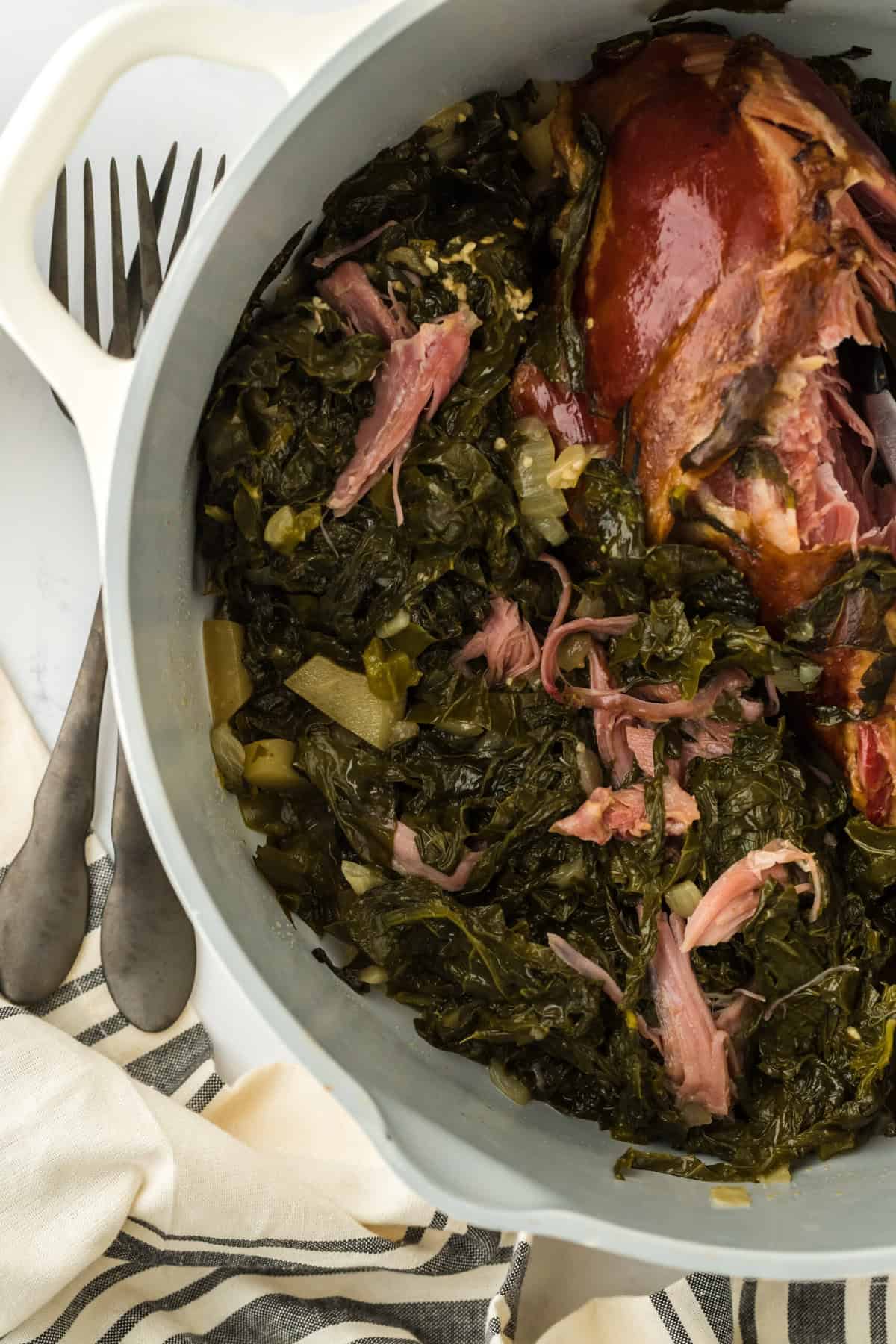 A large white pot of turnip greens with smoked turkey after cooking on a white background