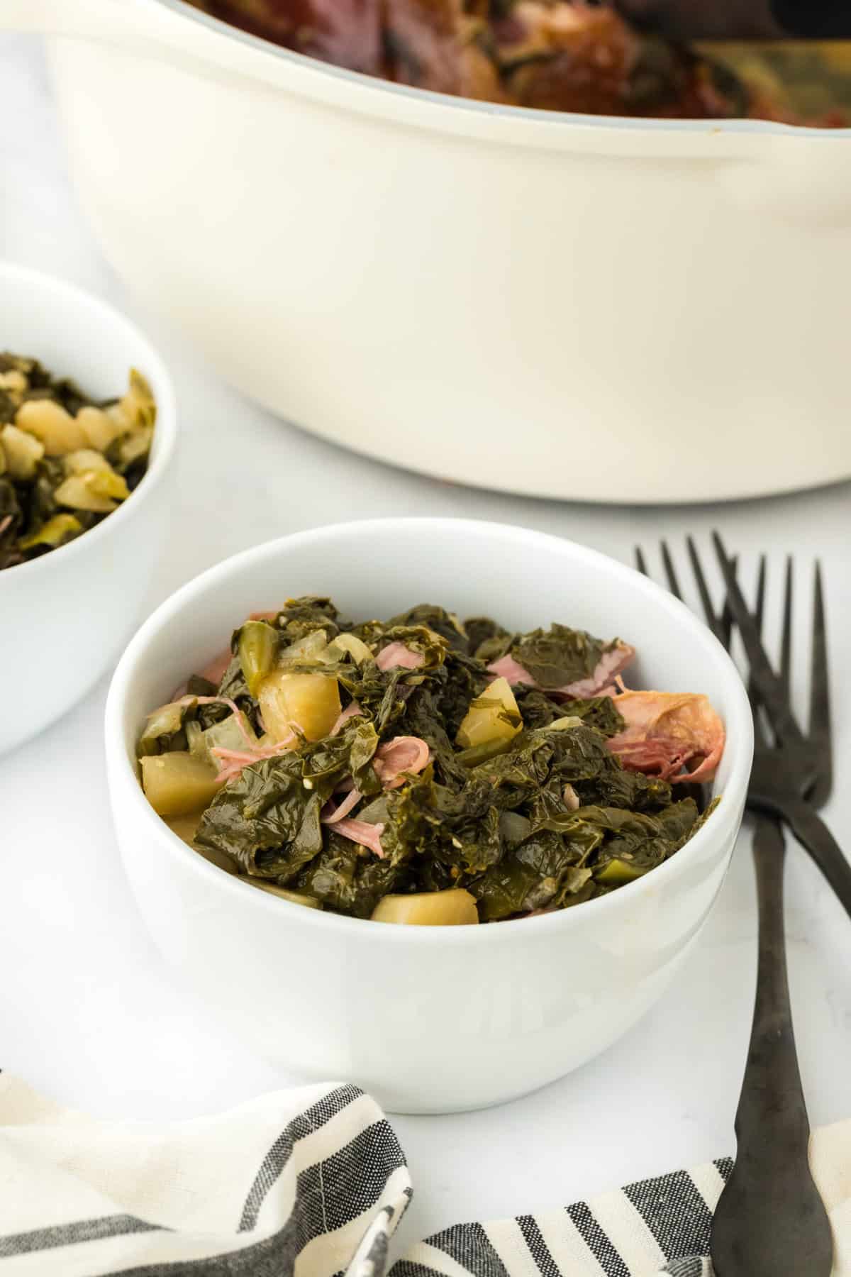 Small white bowls filled with Southern turnip greens with forks nearby