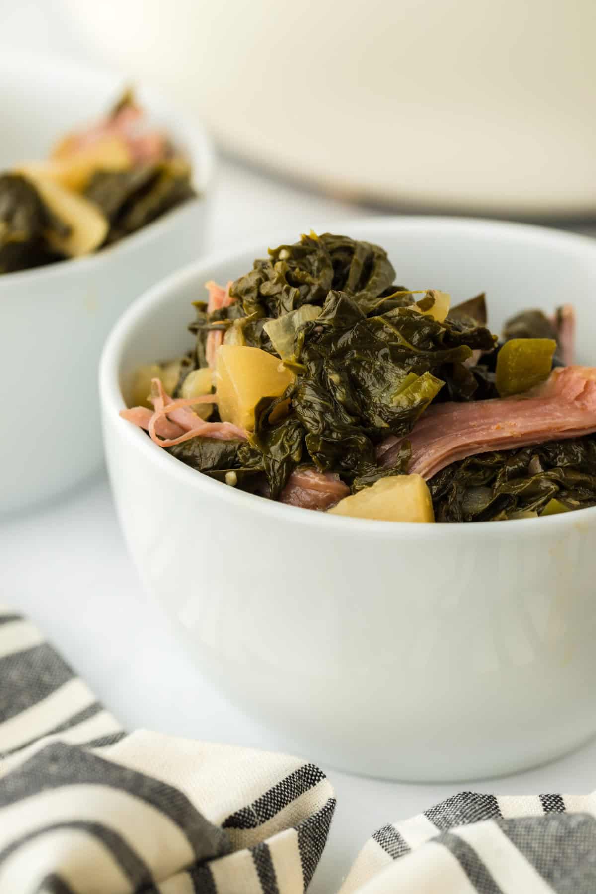 A close up of a white bowl with Southern braised turnip greens recipe being lifted up