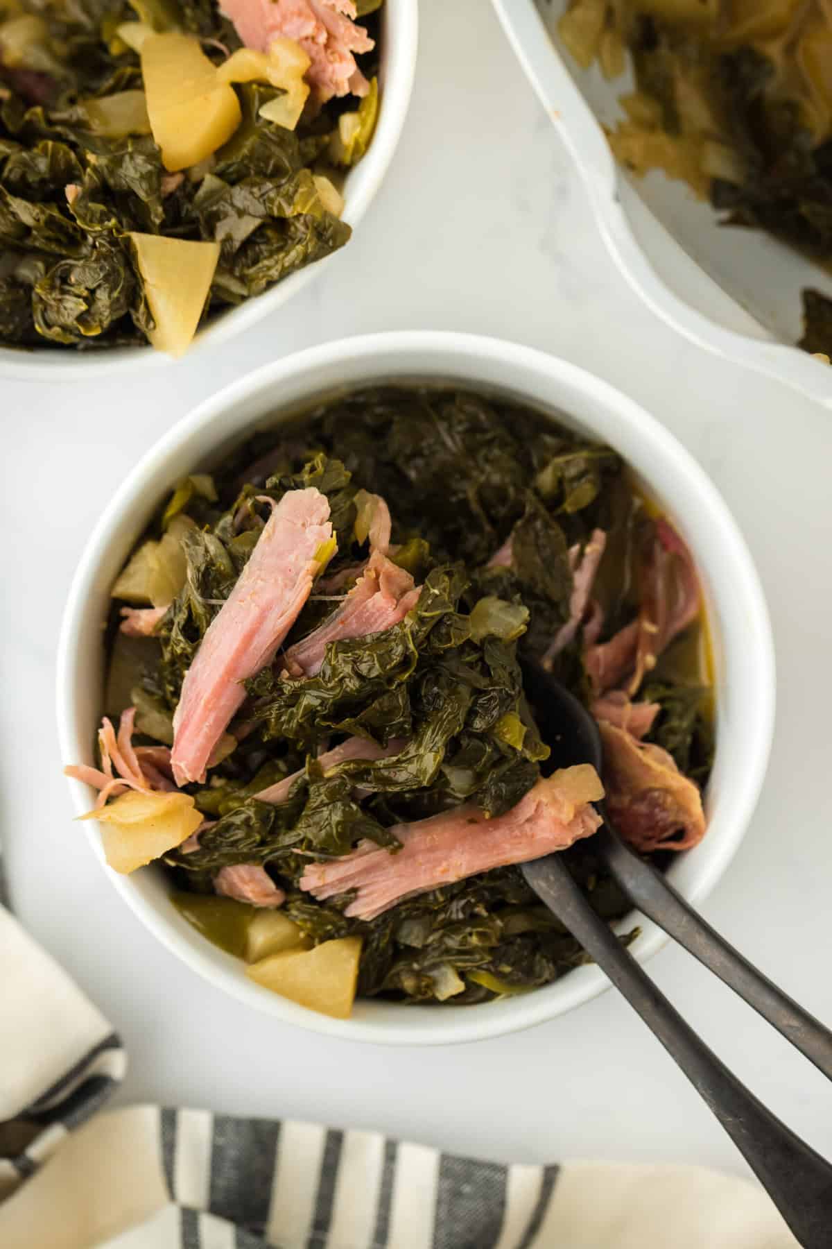 Two small white bowls filled with cooked turnip greens on a white background