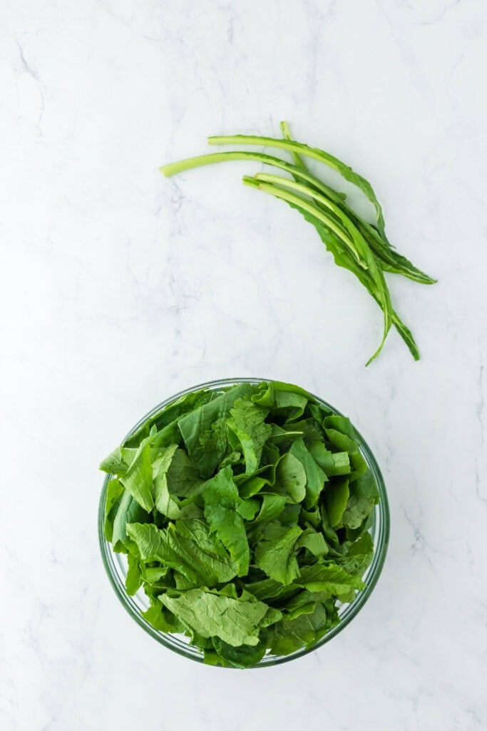fresh greens after being pulled from stems in a clear bowl on white background