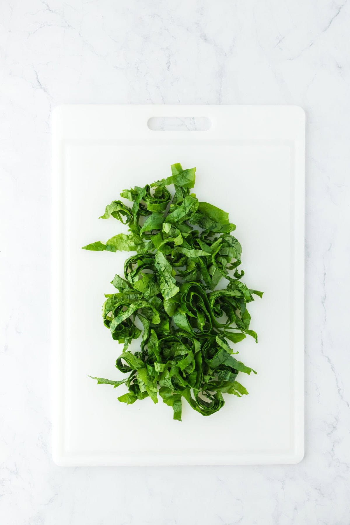 Turnip greens cut in small slivers on a white cutting board