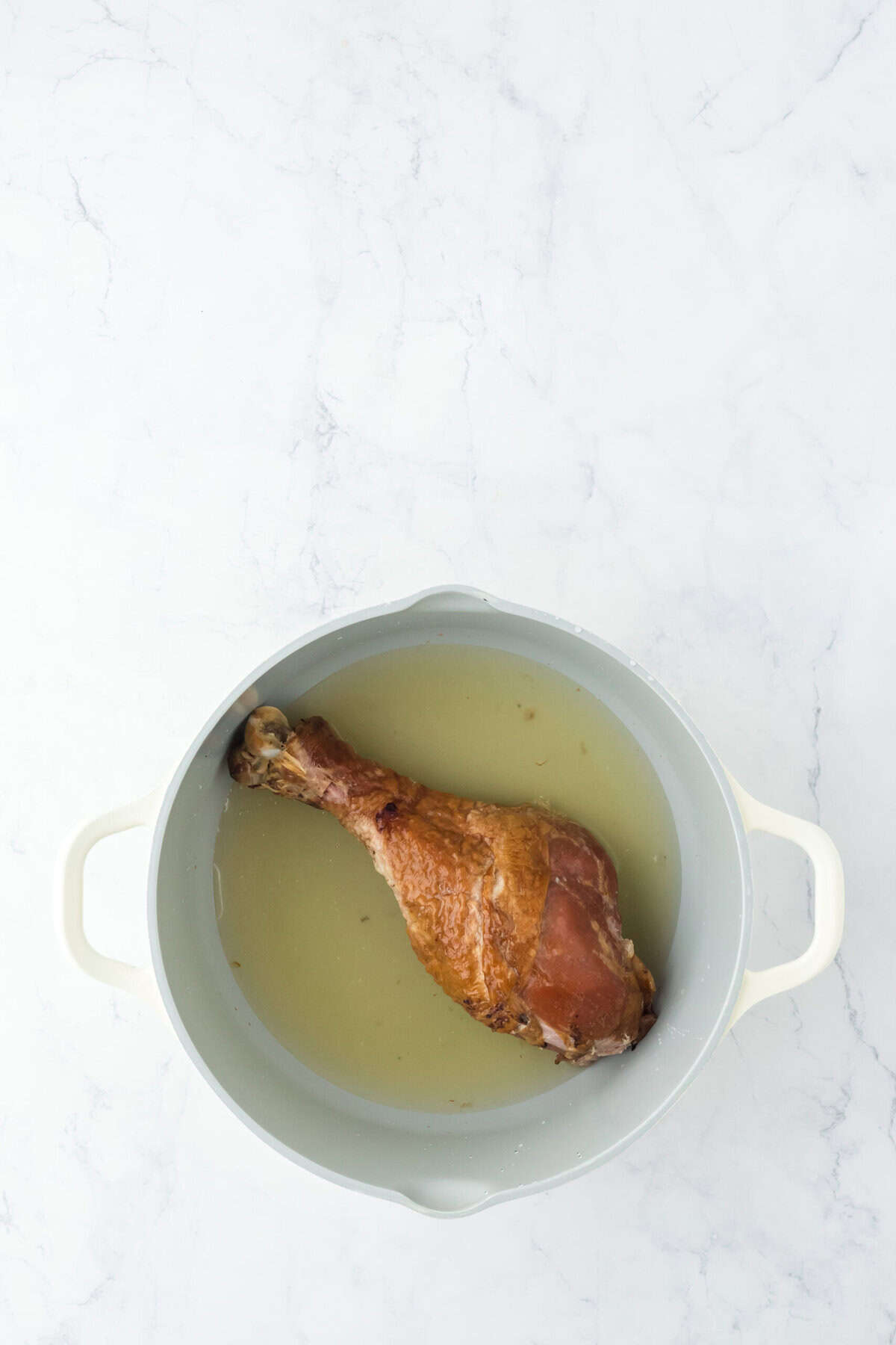 Turkey leg in water and chicken broth in big pot on white background