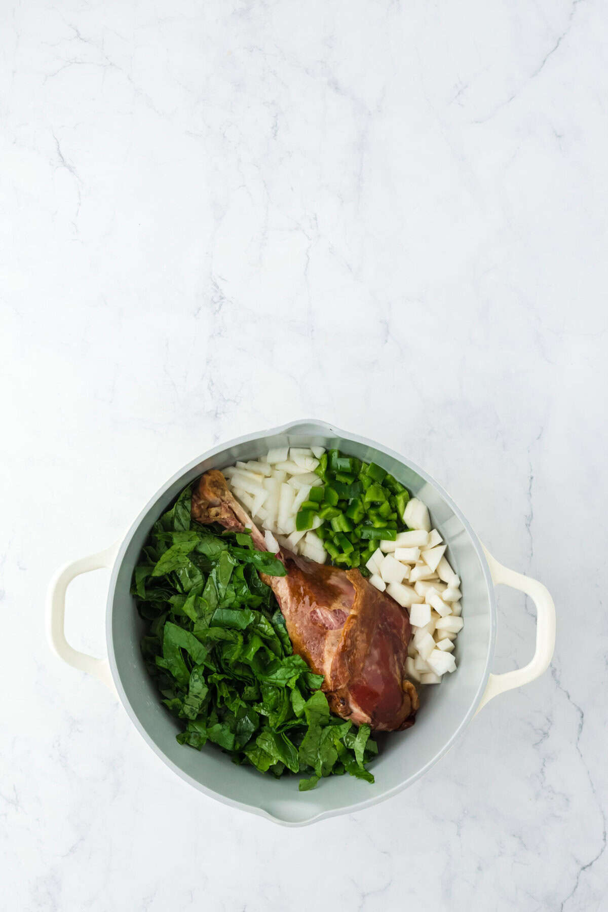 Seasonings and veggies added to pot with turkey leg on white background