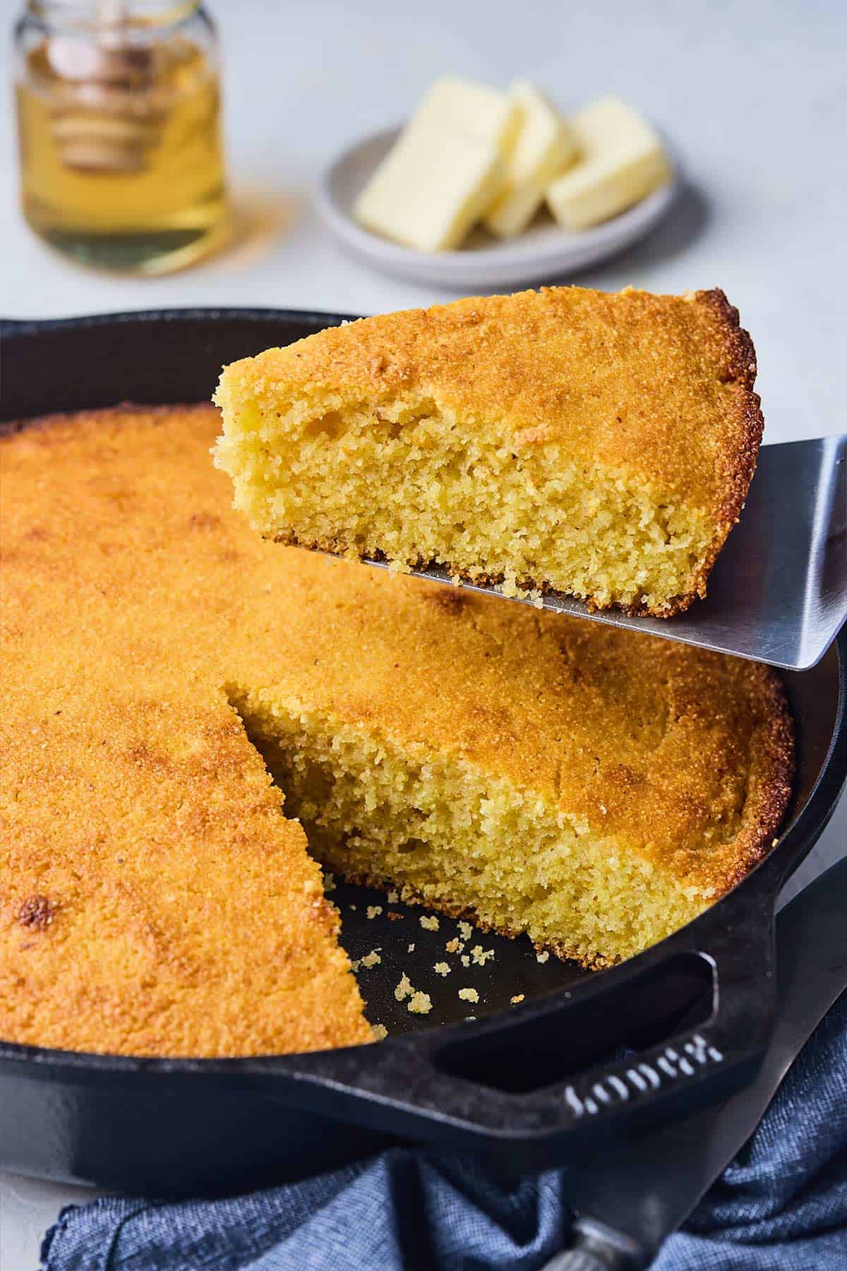 Close up shot of a honey cornbread recipe slice lifting from black, cast iron skillet