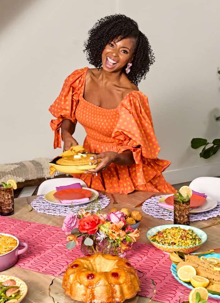 Jocelyn Delk Adams in orange dress serving dinner at colorful table
