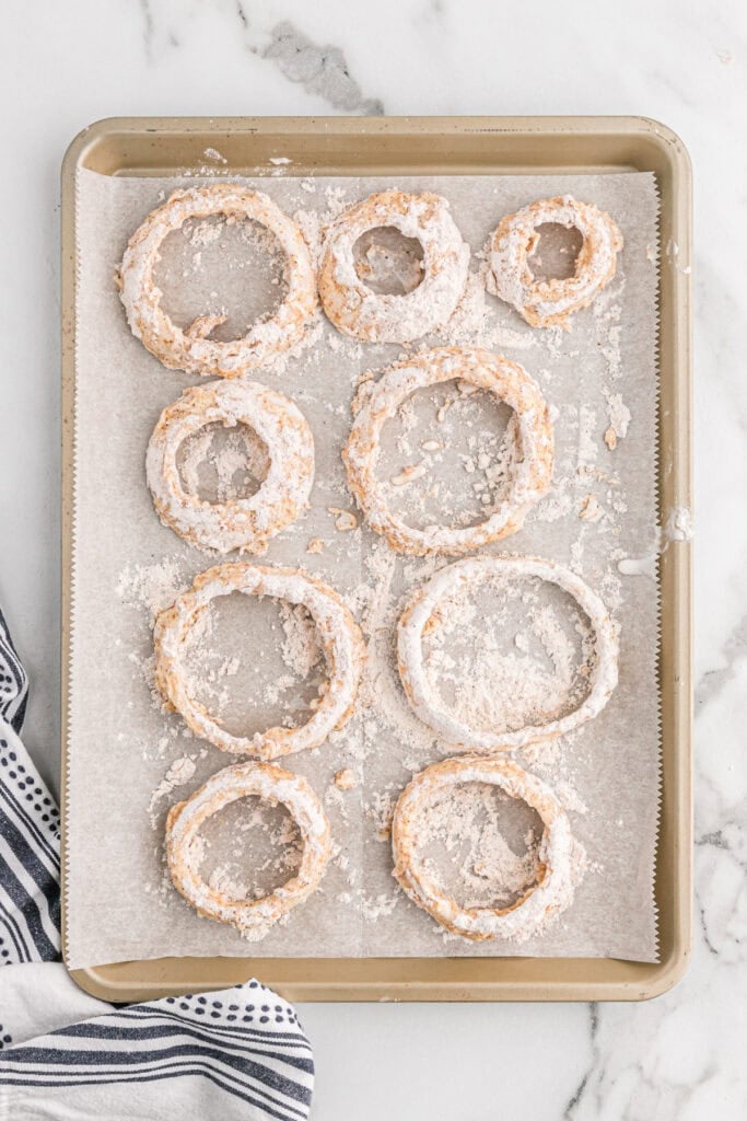 Sliced onion rings that are breaded on a sheet pan before frying