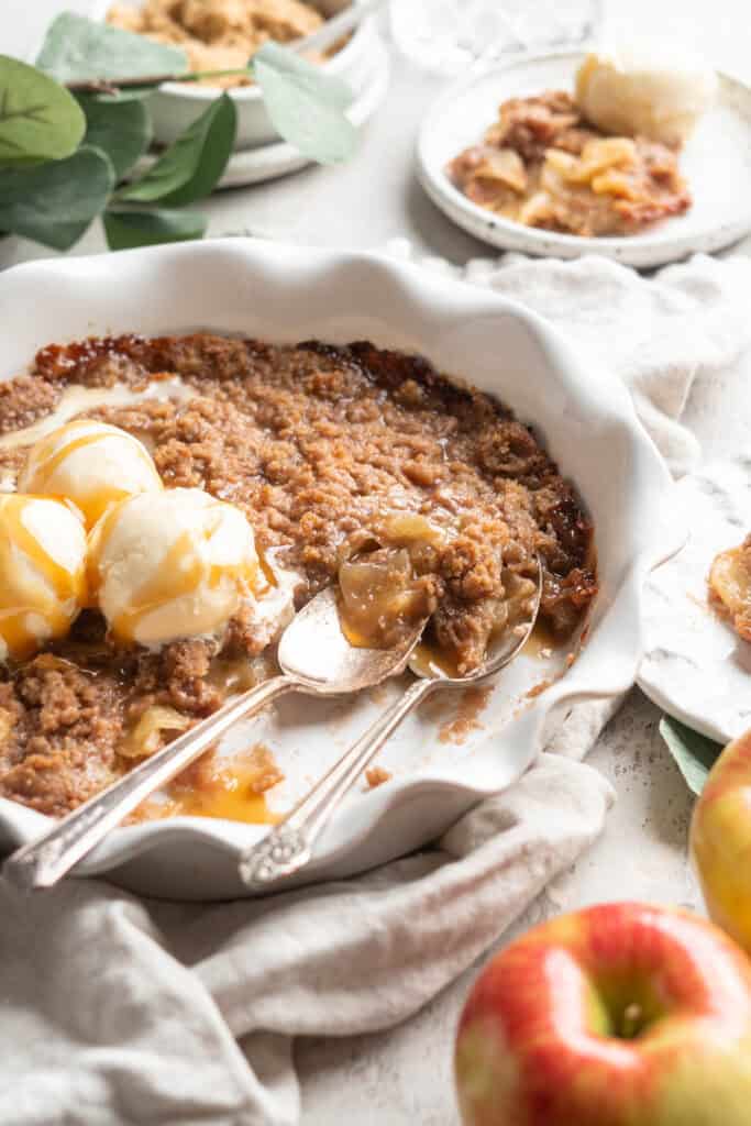 brown apple betty being served with ice cream and caramel drizzled on top