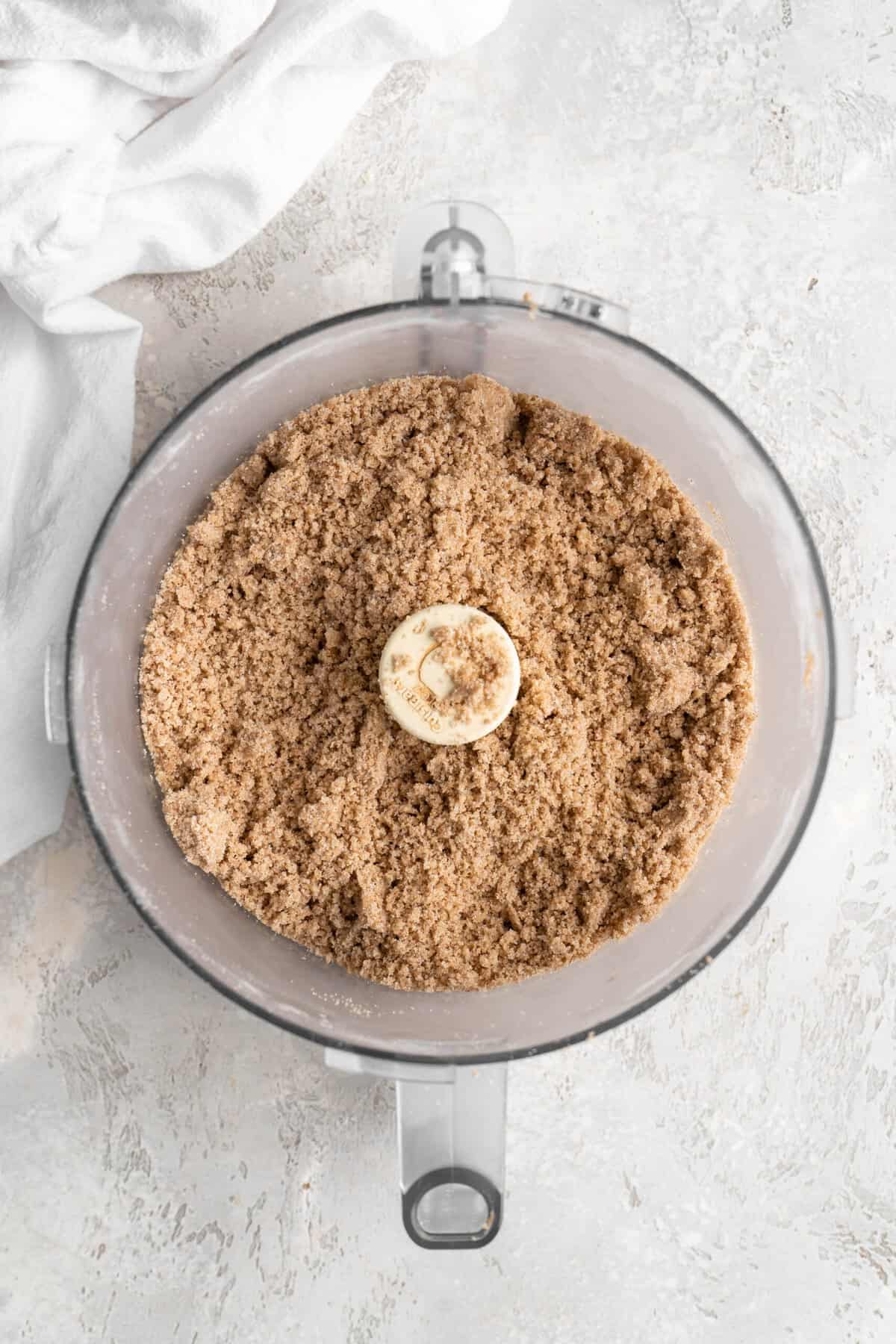 Crumble added to a food processor on a white background