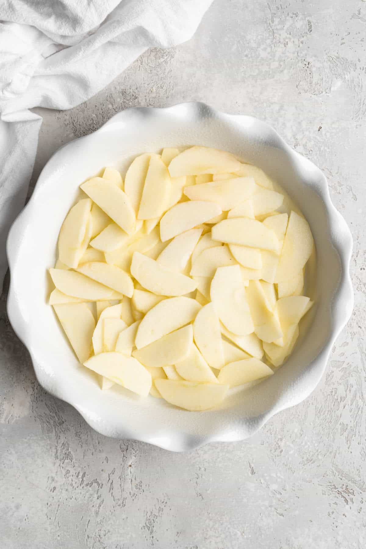 Apple slices tossed with lemon juice added to a white baking dish.