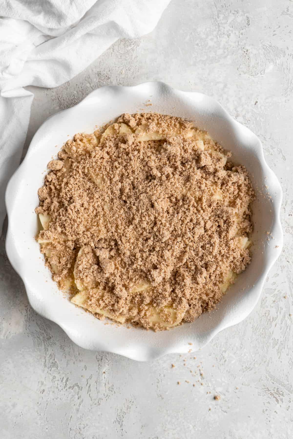 Brown sugar crumble layered over half of apple slices in a white baking dish