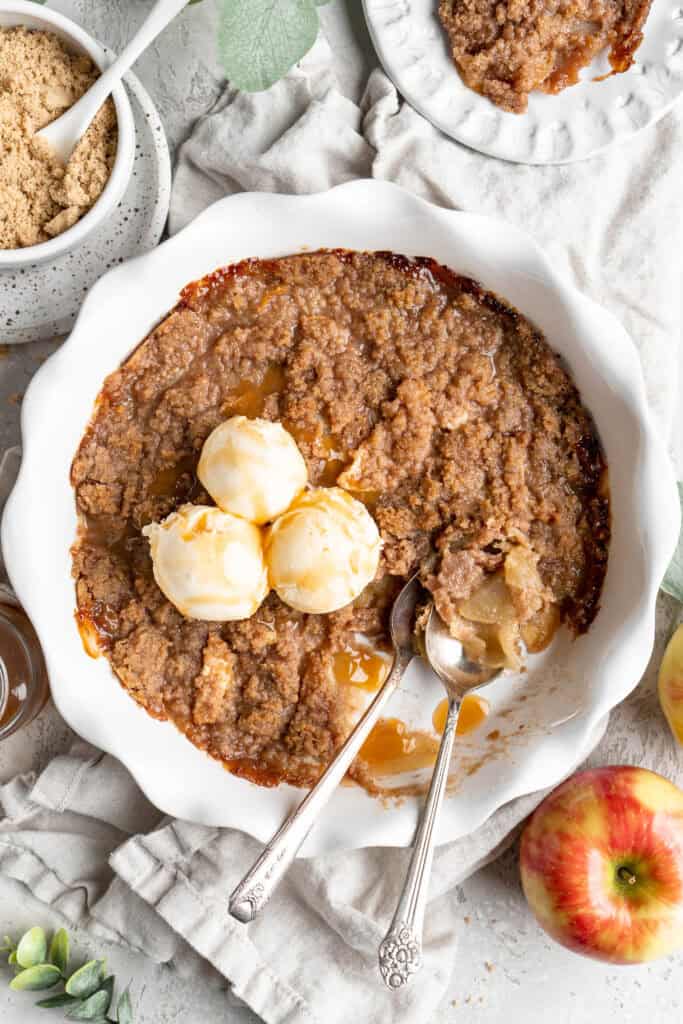 Apple brown betty recipe with three scoops of vanilla ice cream on white background with apples and crumble in the background