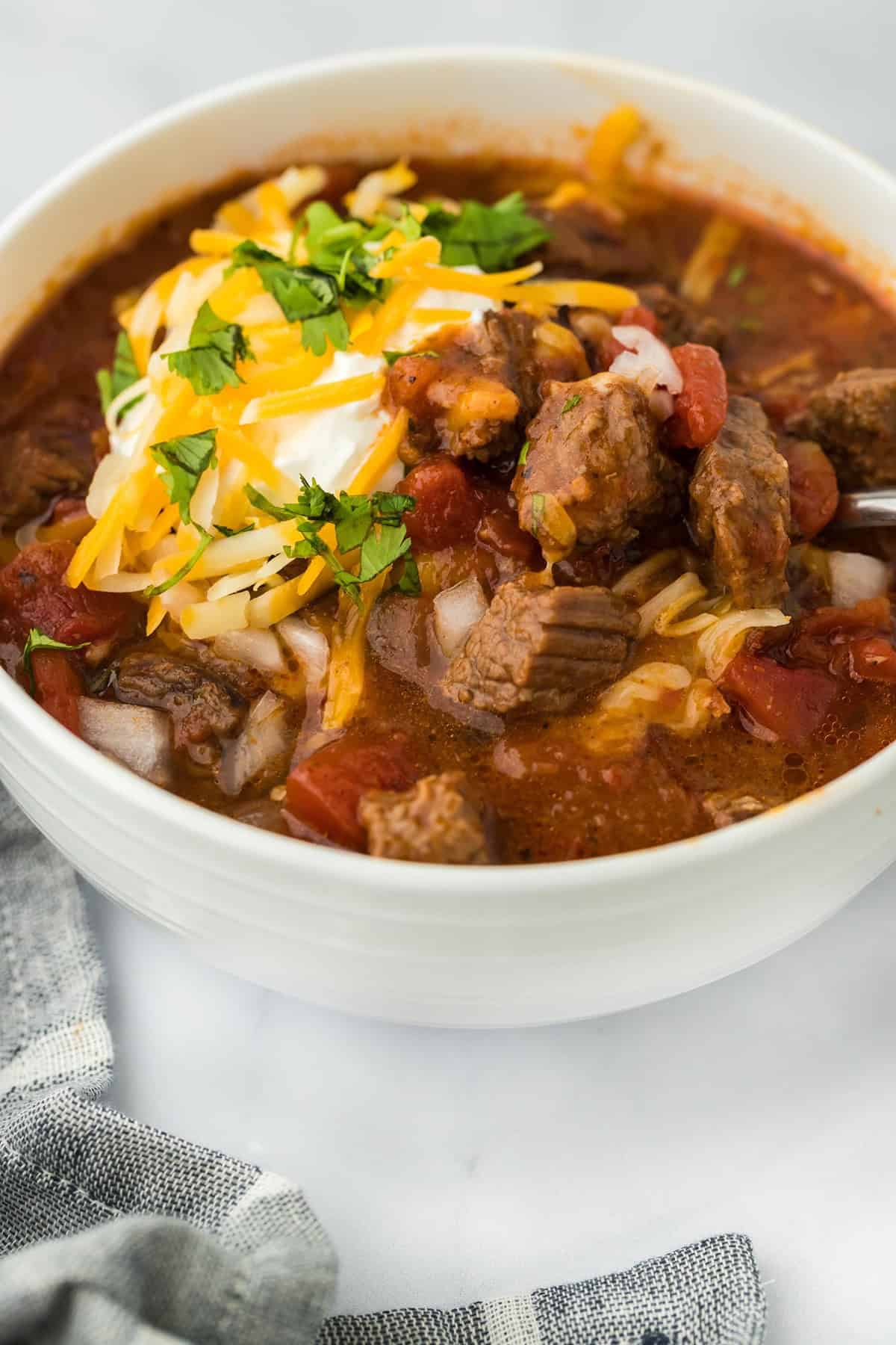 Closeup of a bowl of brisket chili topped with shredded cheese, sour cream, and cilantro