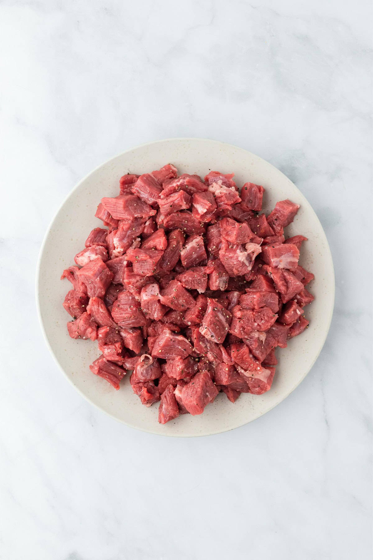 A plate of raw, cubed brisket seasoned with salt and pepper