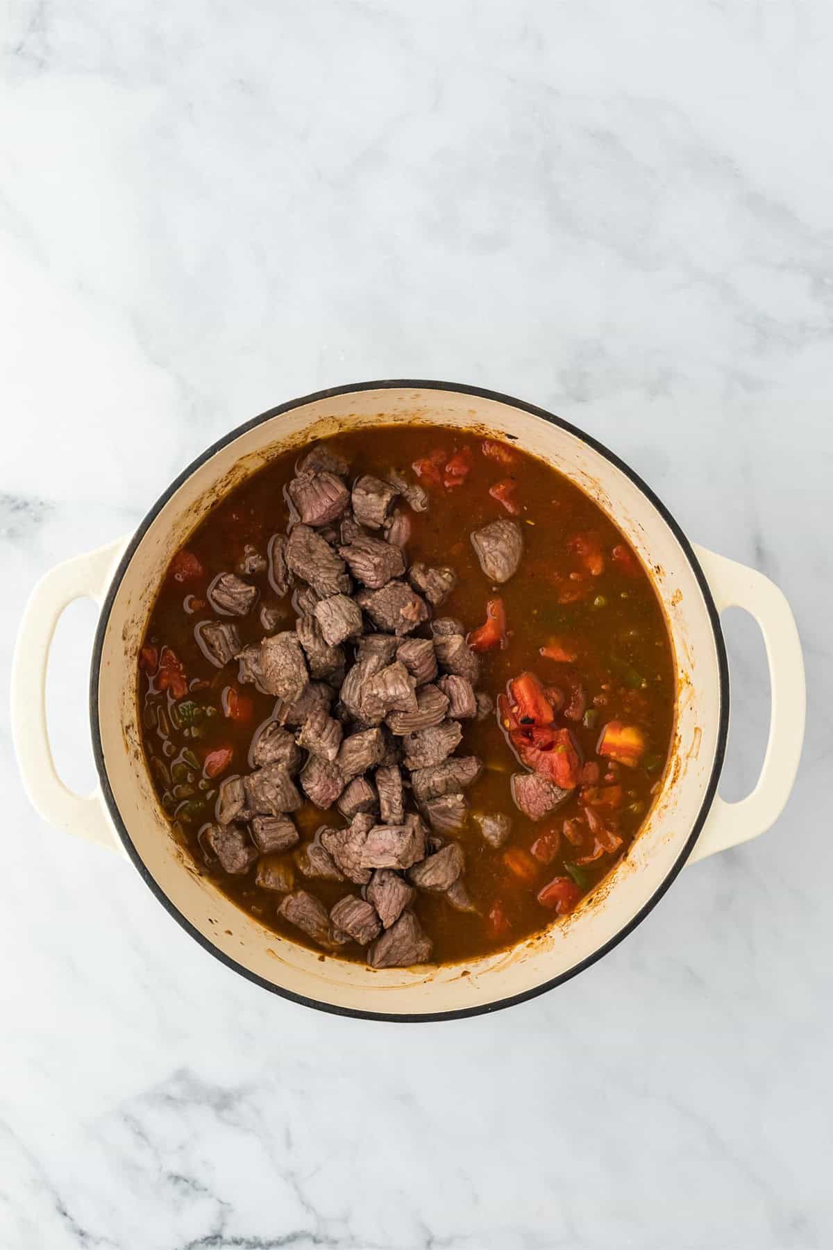 Cooked brisket cubes returned to the Dutch oven, mixed with the chili base