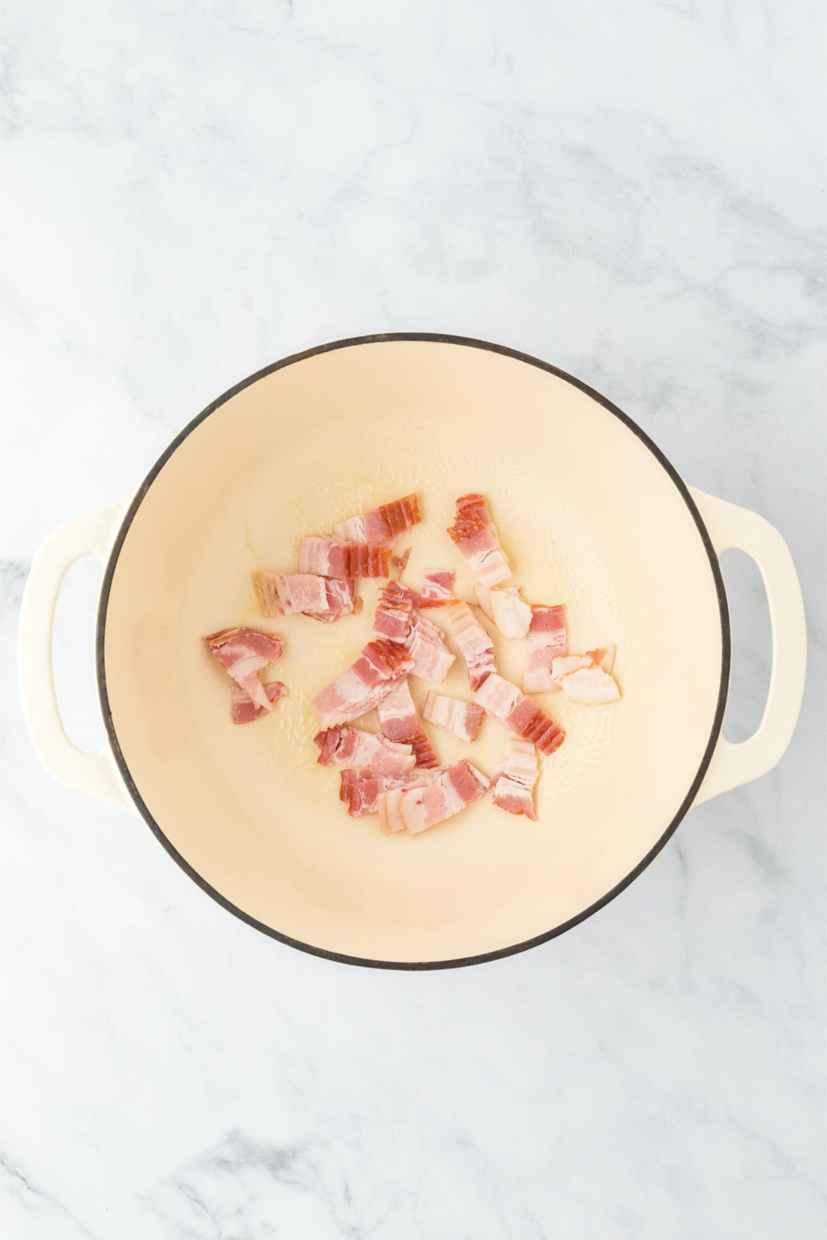 A Dutch oven with bacon pieces starting to cook at the bottom