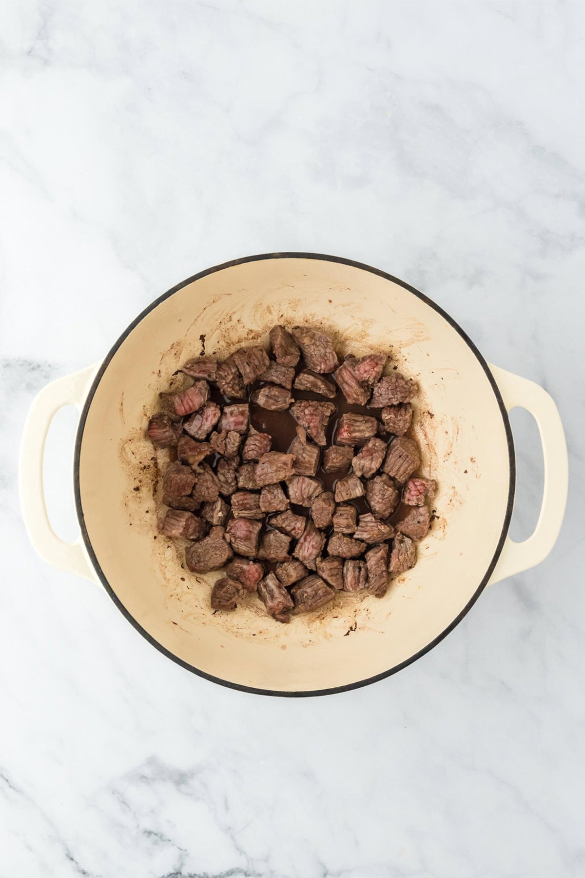 Cubes of brisket after browning in a large, white Dutch oven