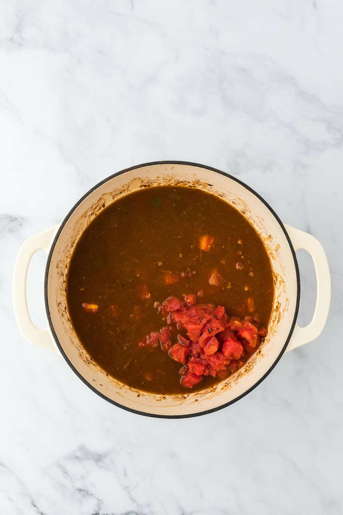 Tomatoes added to the chili base in the Dutch oven