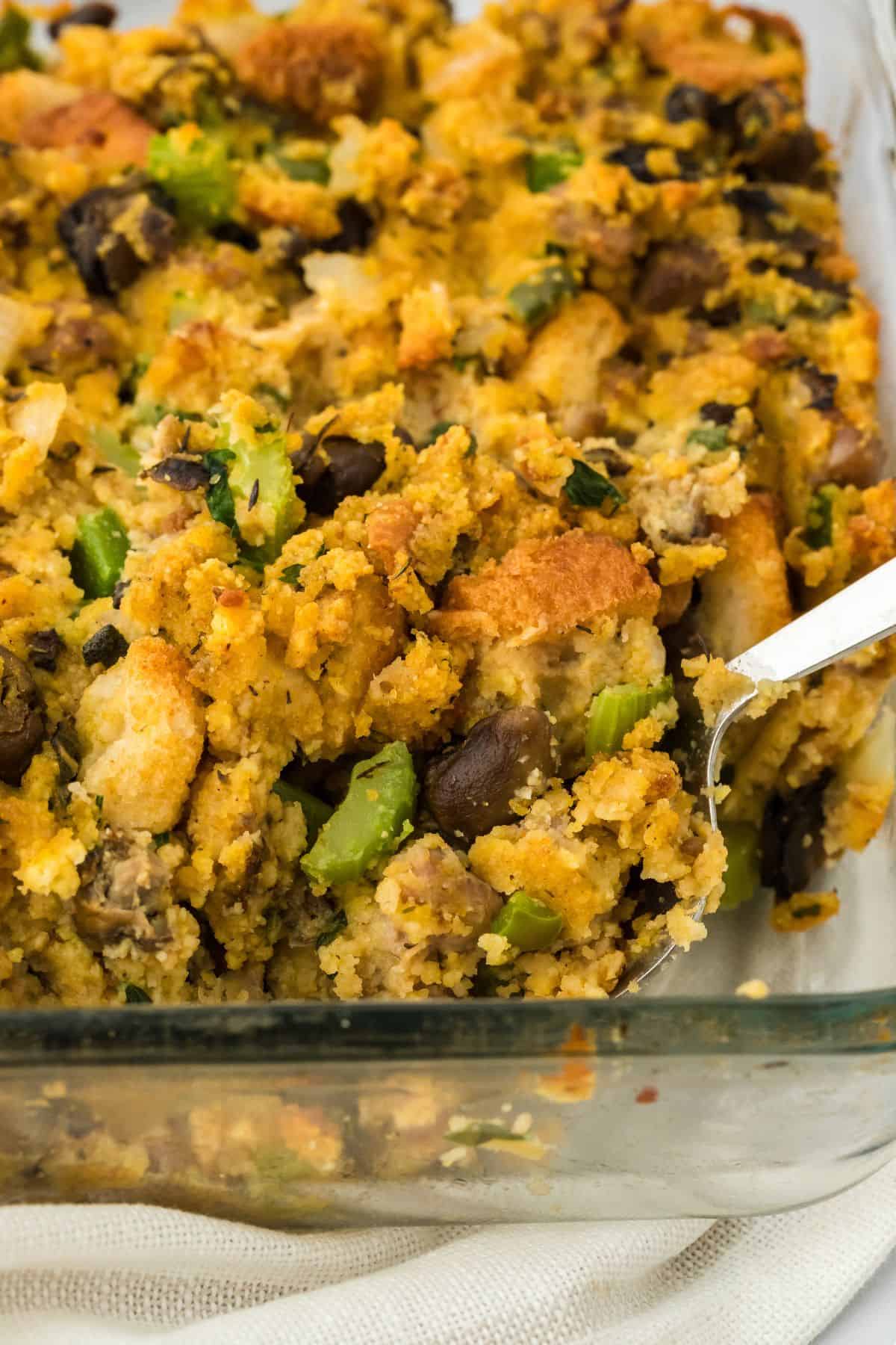 Closeup of oyster dressing in a glass baking dish with a spoon in it lifting a portion