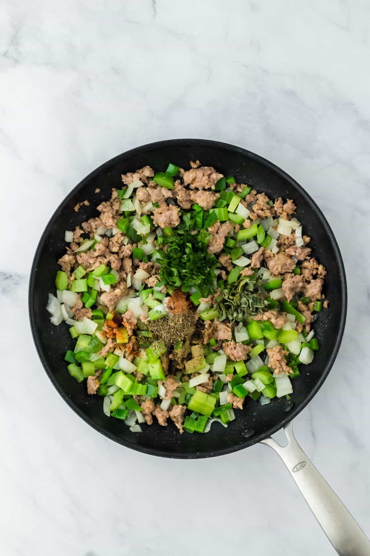 Sausage and vegetables cooking together in the skillet, with herbs and spices added on top