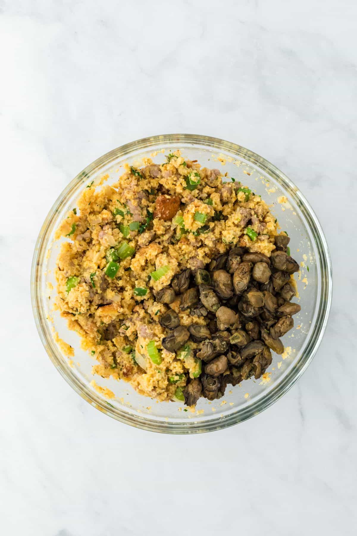 A large mixing bowl with cornbread, crouton crumbs, sausage mixture, and a pile of oysters on the side