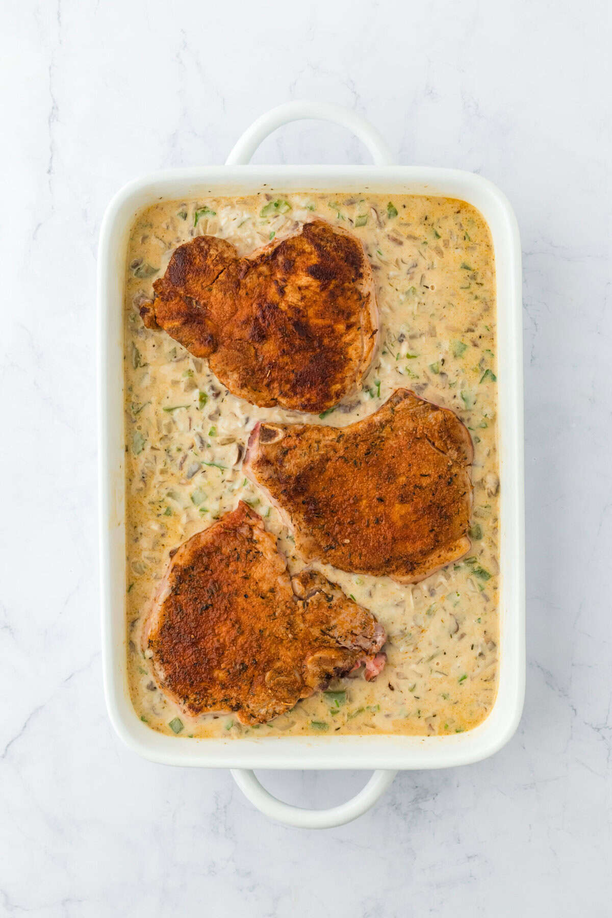 pork chop casserole before baking with 3 pork chops on top of the rice and veggie mixture