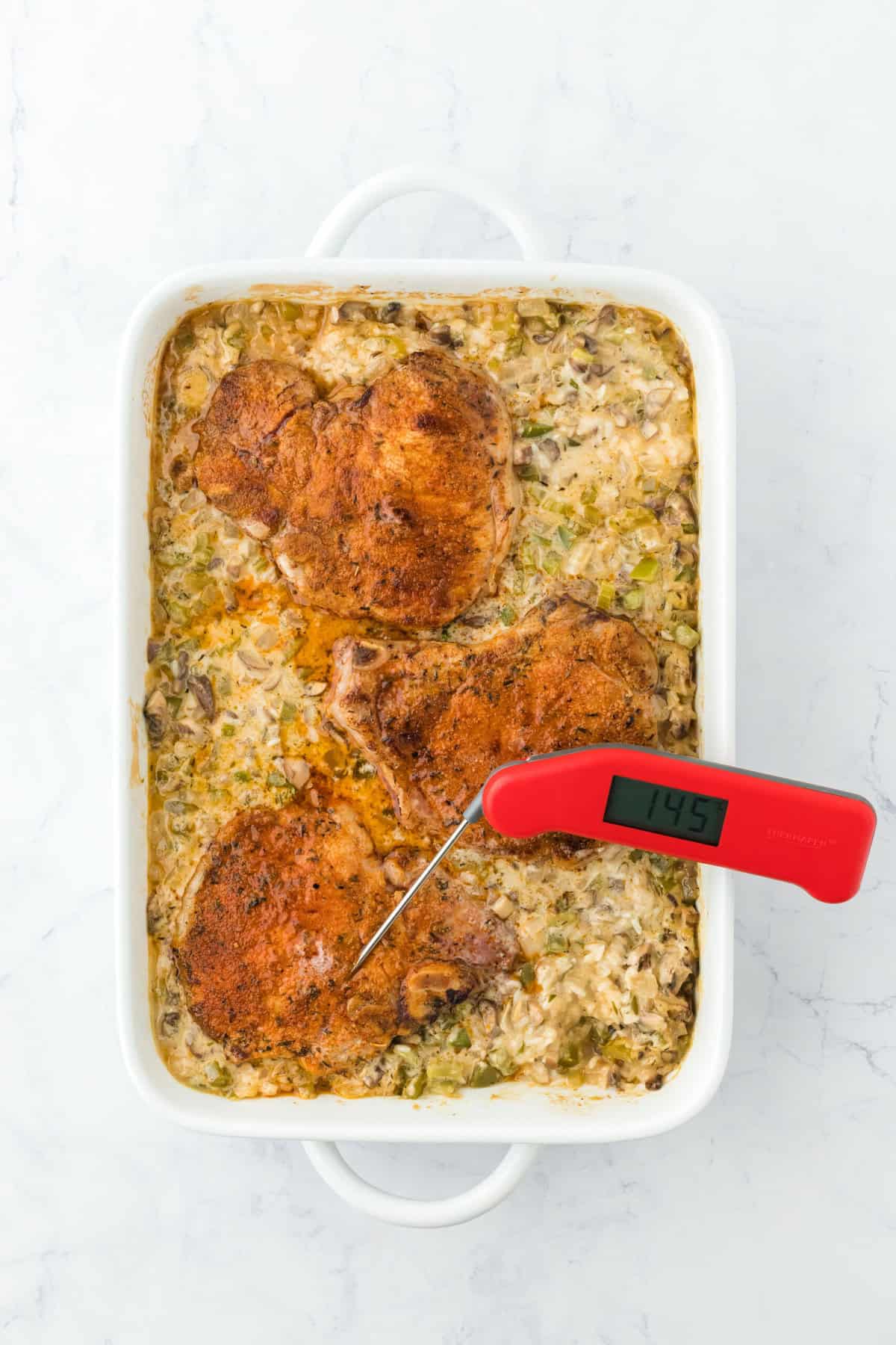 a meat thermometer sticking out of a pork chop in the casserole dish to check it's doneness