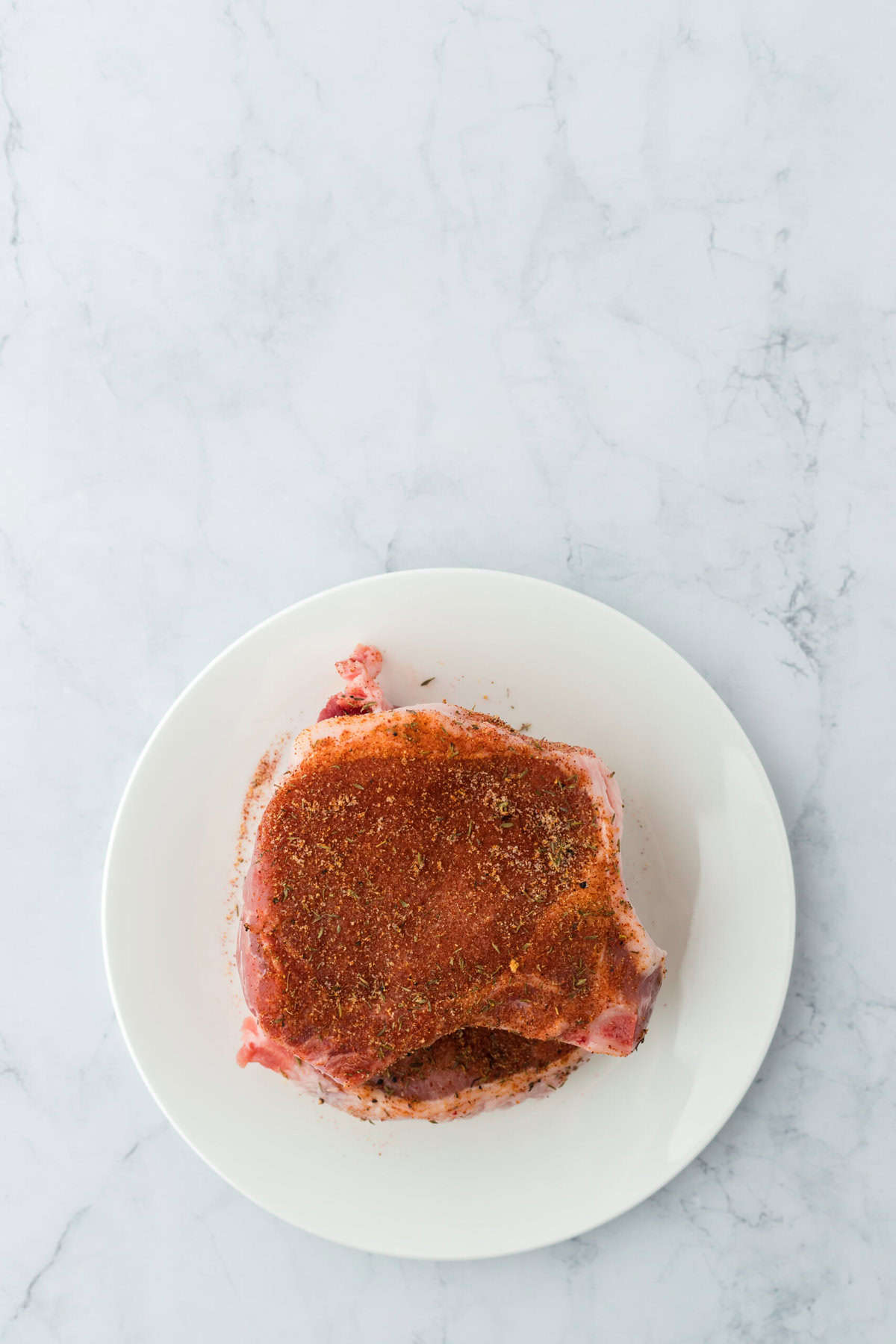 overhead view of a raw porkchop after it's been seasoned