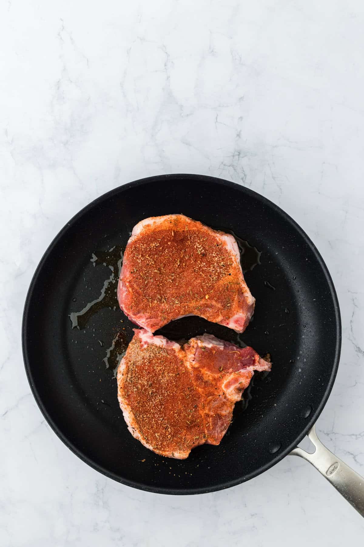 two raw pork chops added to a skillet to brown the outside