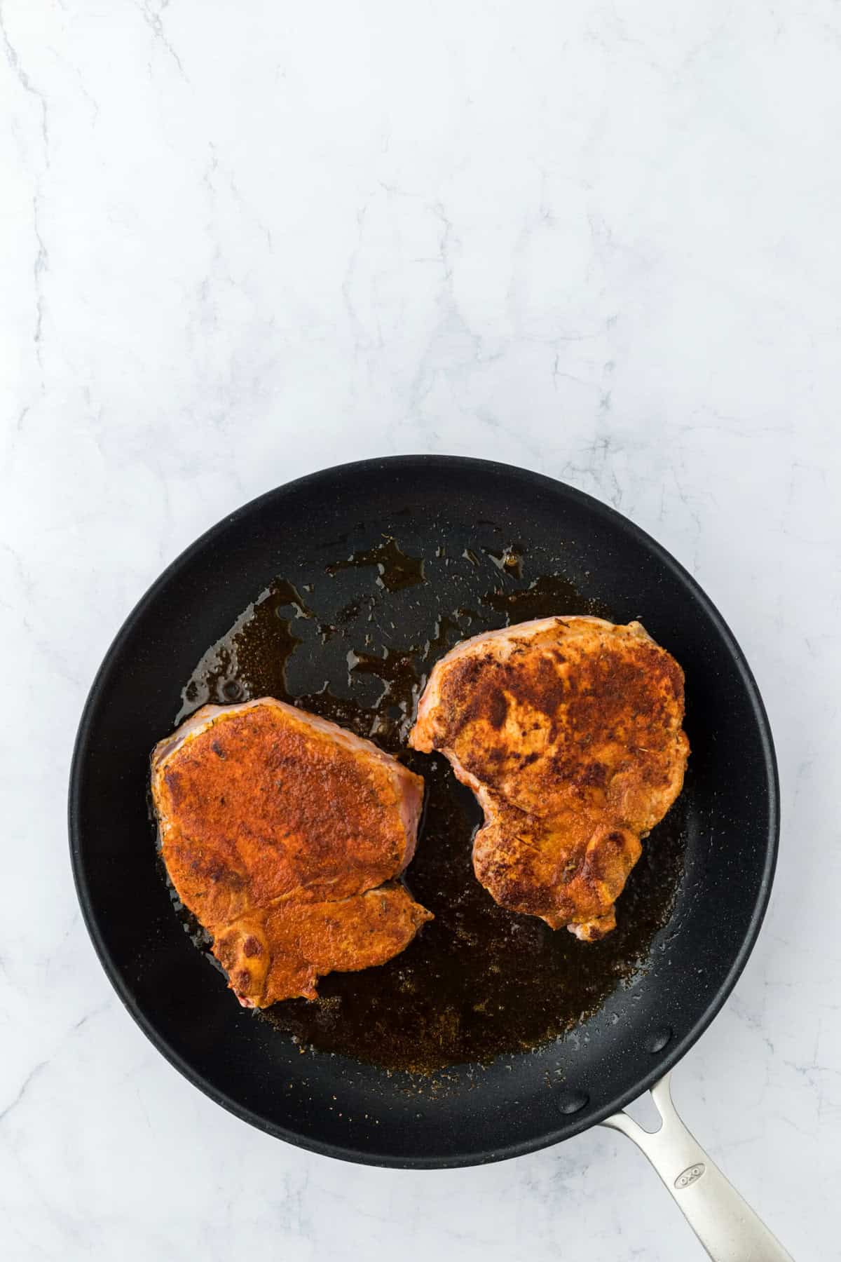 two pork chops in a skillet being seared