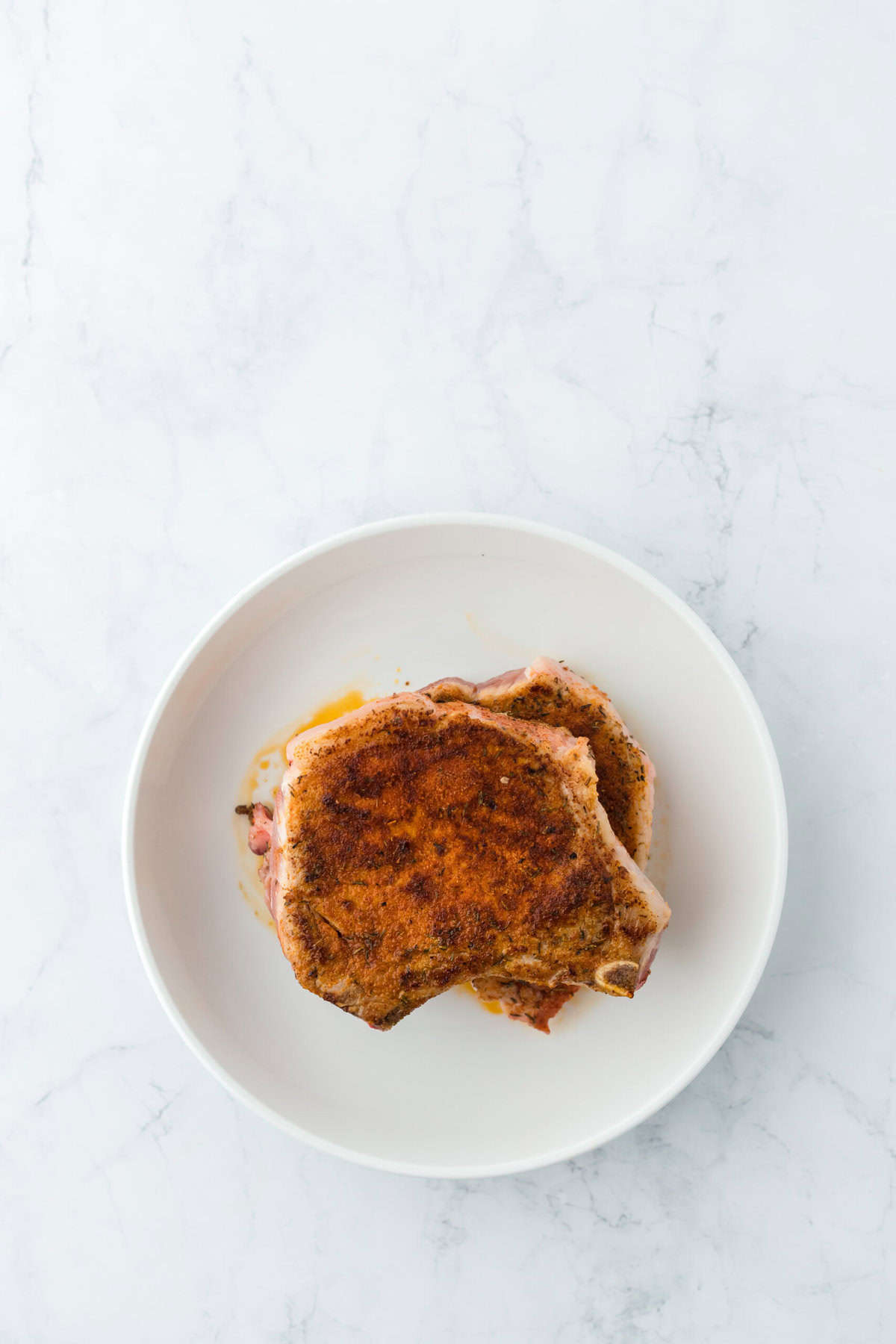 two porkchops stand on a plate one on top of the other after being seared on each side for pork chop casserole