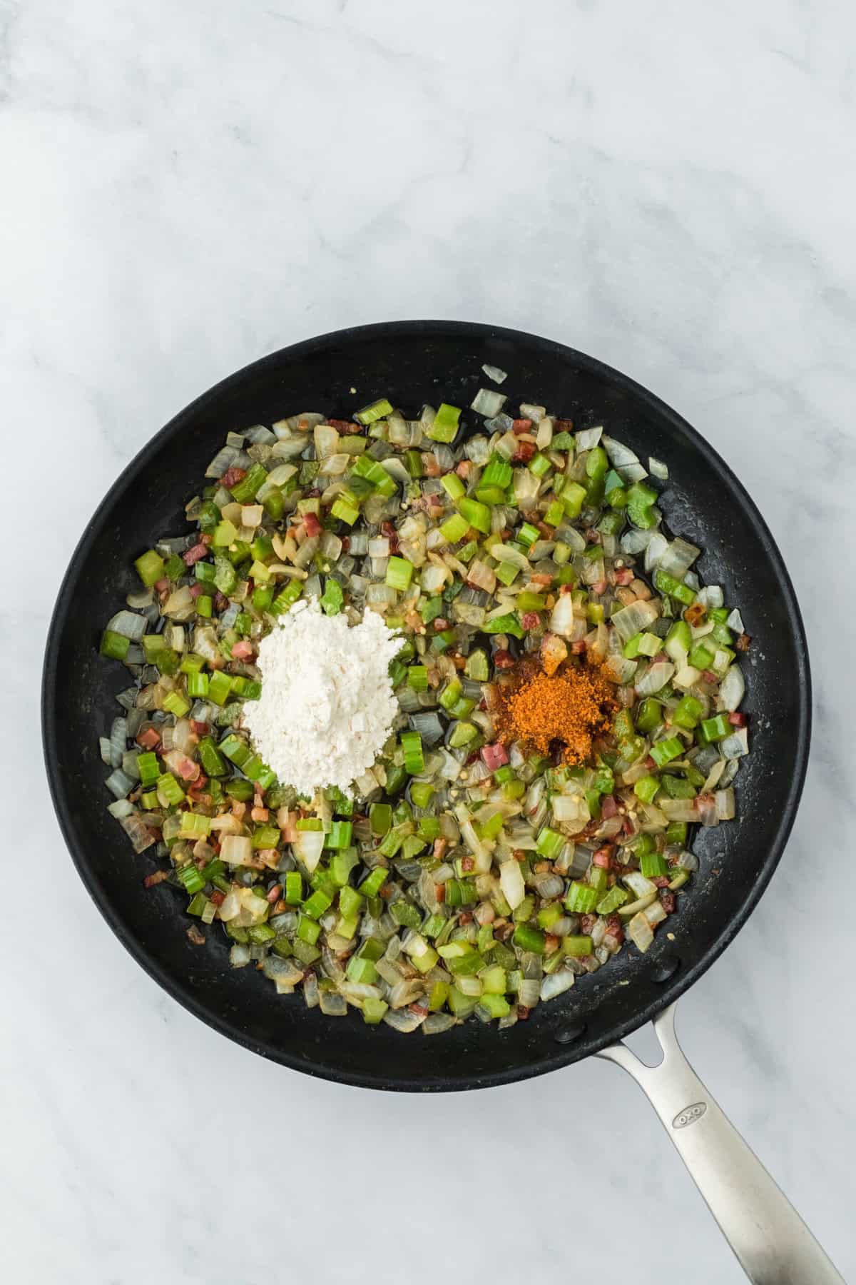 Flour and creole seasoning in a pan with sauteed veggies.