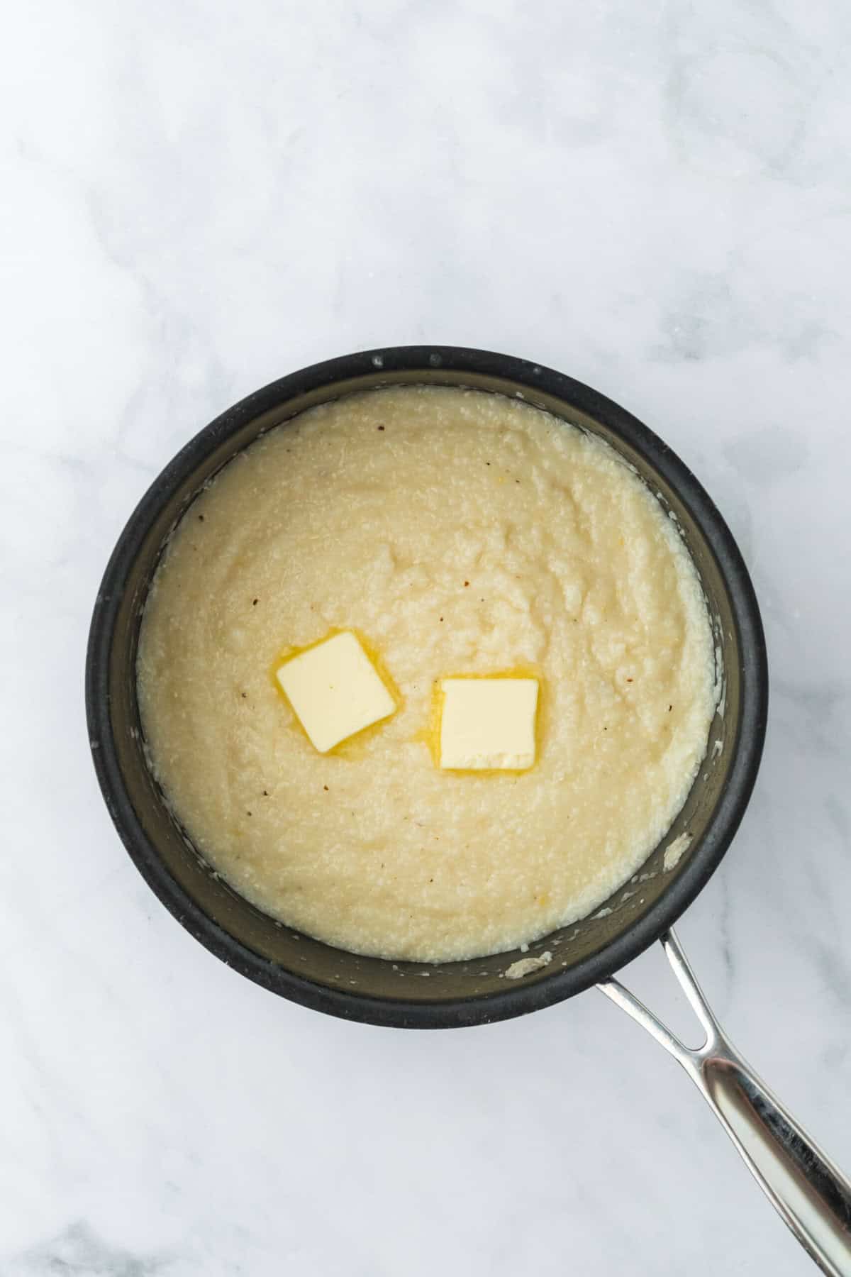 Two butter pats on saucepan filled with cooked grits