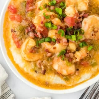 A large white bowl of shrimp and grits with two forks nearby on white countertop