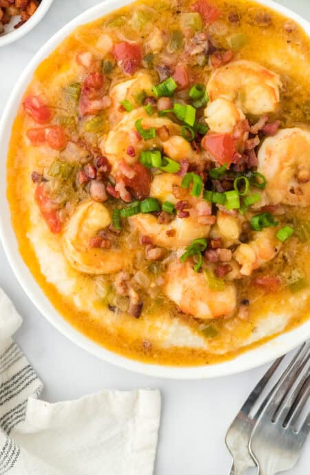 A large white bowl of shrimp and grits with two forks nearby on white countertop