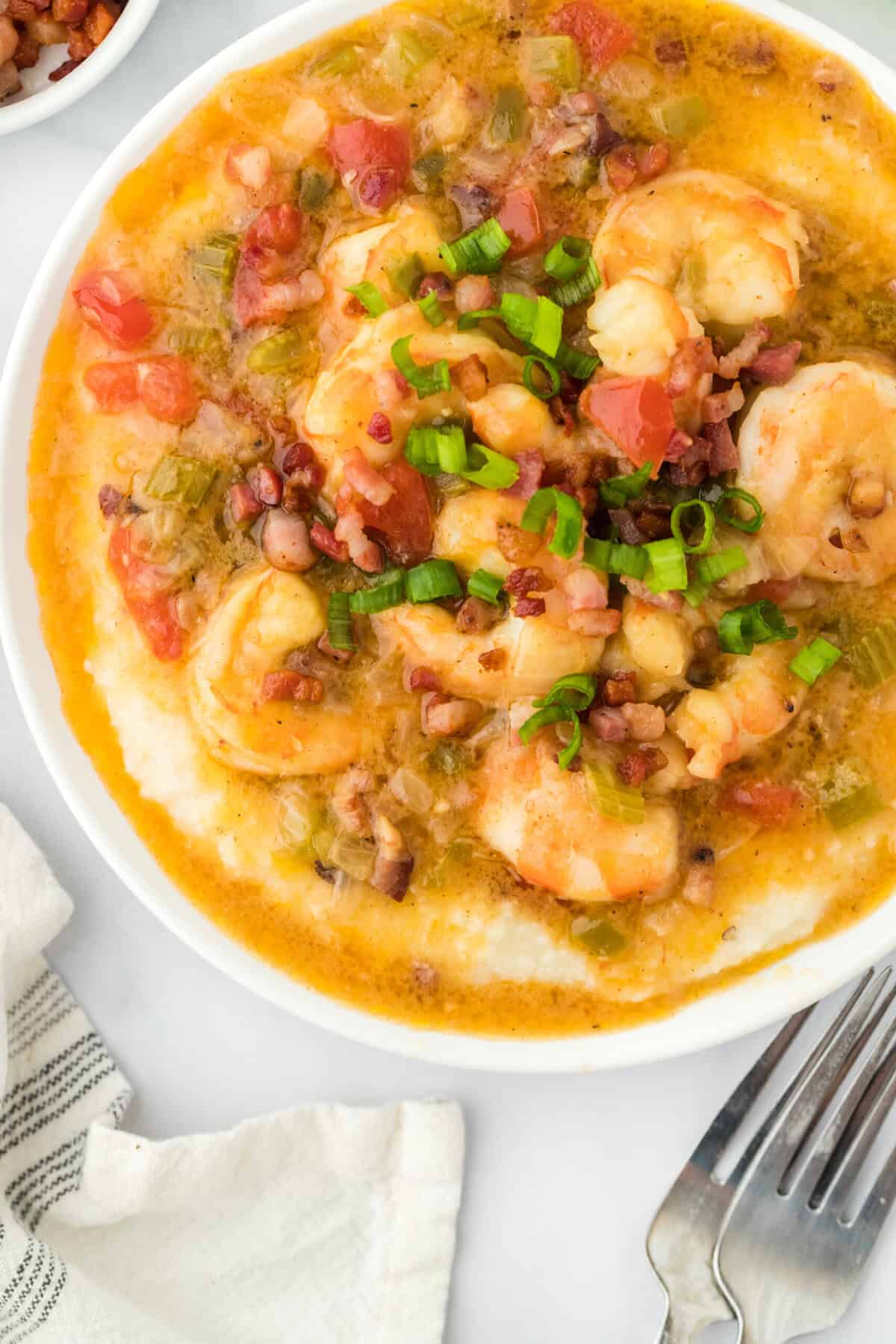 A large white bowl of shrimp and grits with two forks nearby on white countertop