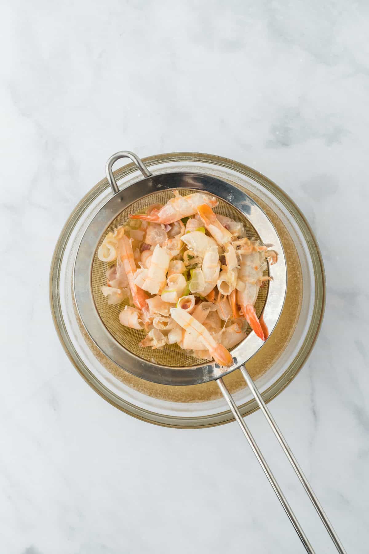 Shrimp stock being strained over container on white countertop