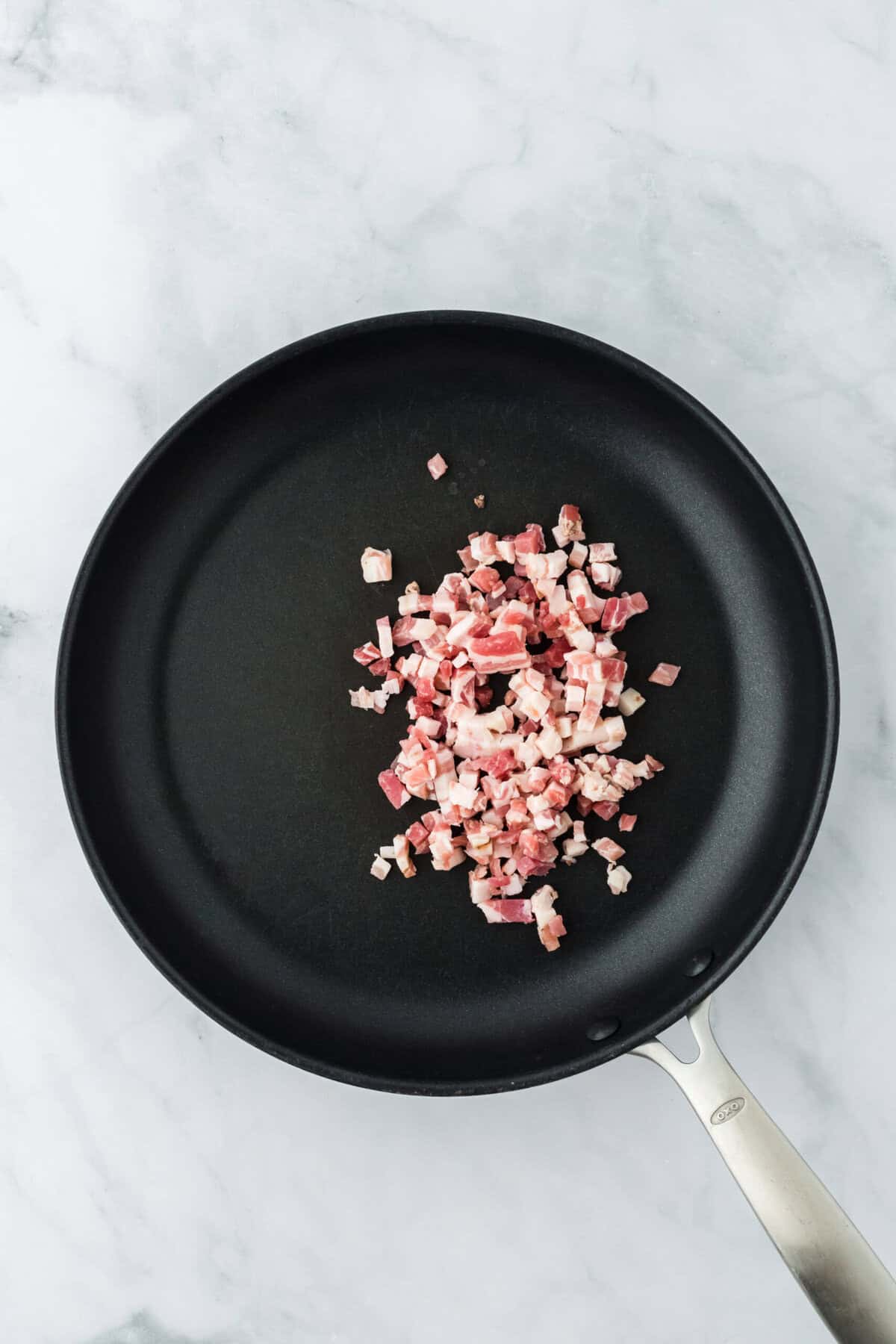 Pancetta added to a pan on white countertop