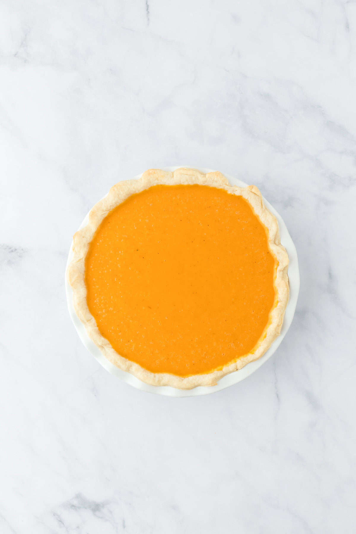 Potato pie filling poured into a pie crust on white background before baking