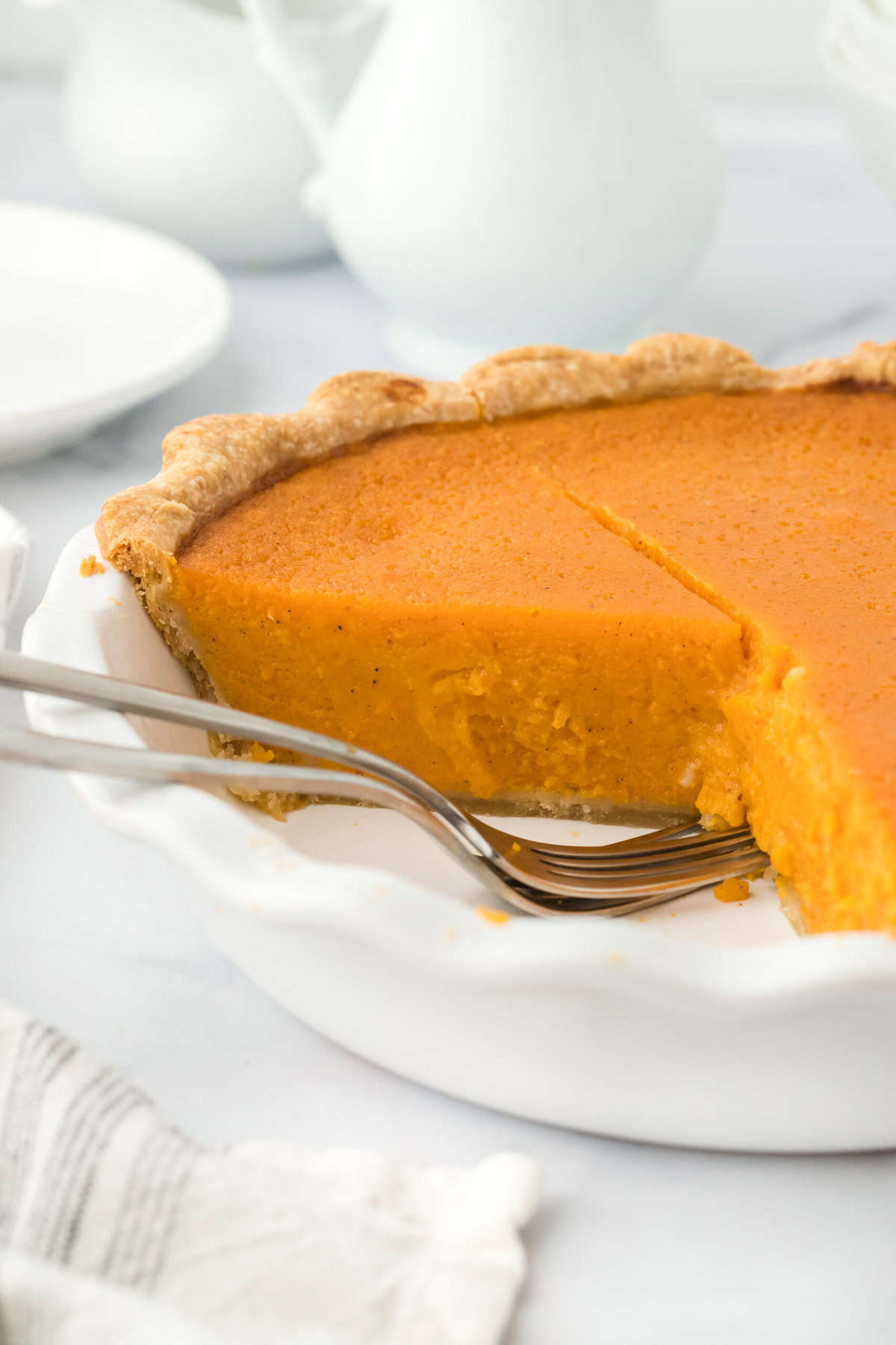 Sliced Southern sweet potato pie with forks on a white countertop with a white plate in background